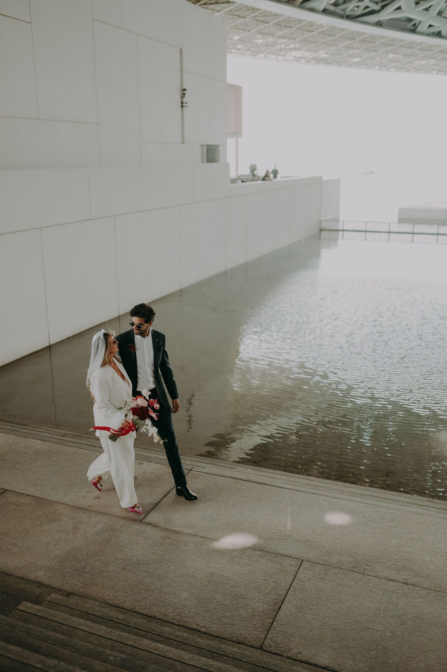 A couple walking through a modern architectural space with white walls and reflective floors.