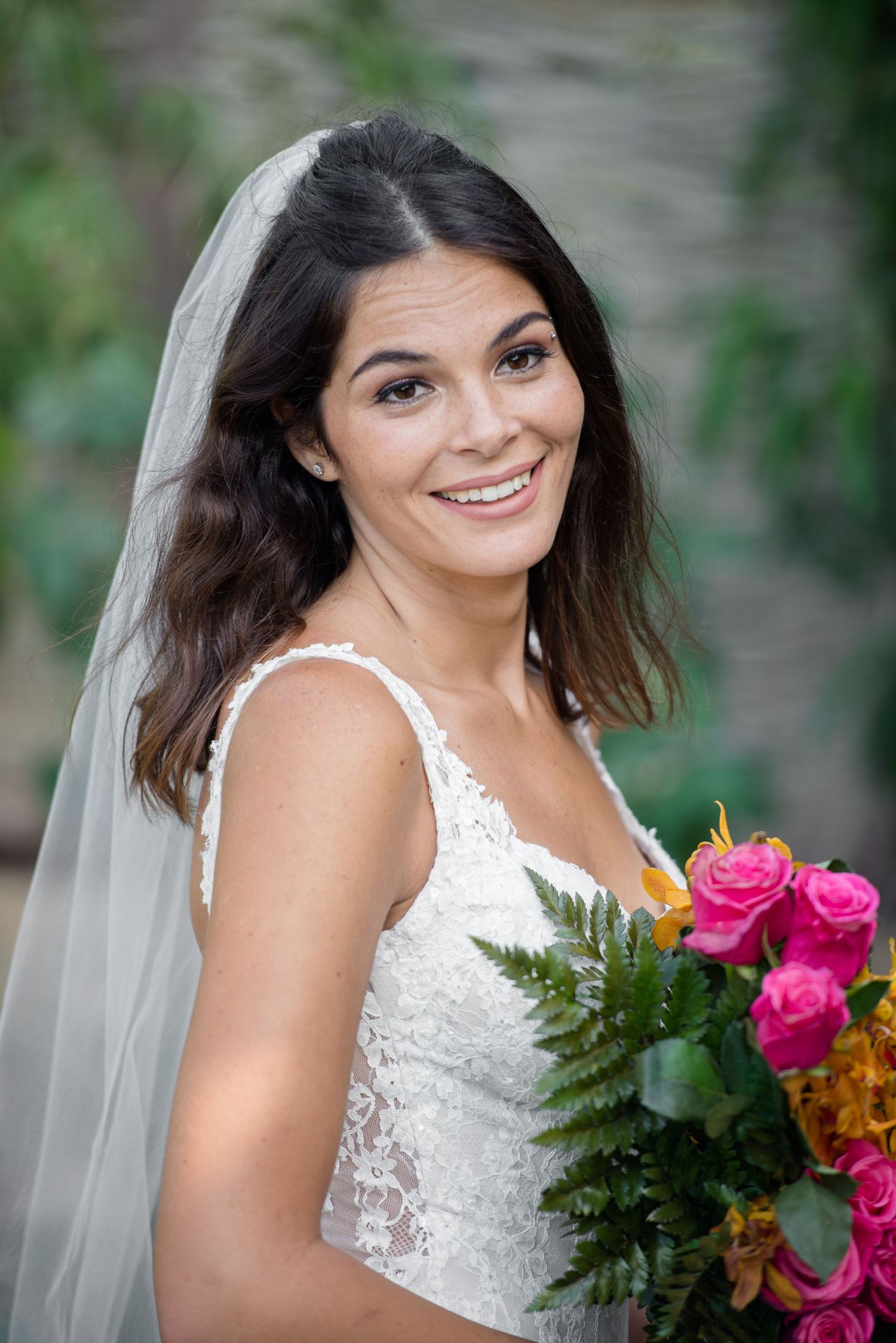A bride wearing a white lace gown holds a bright bouquet of pink and orange flowers.
