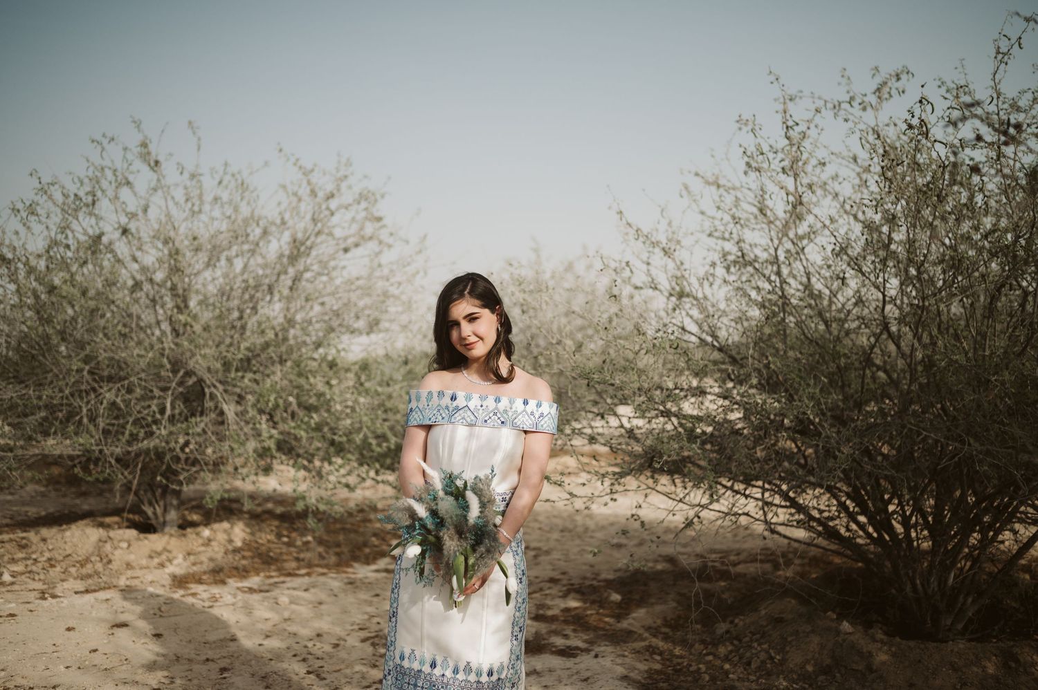 Desert landscape with woman in white dress standing among desert brush.