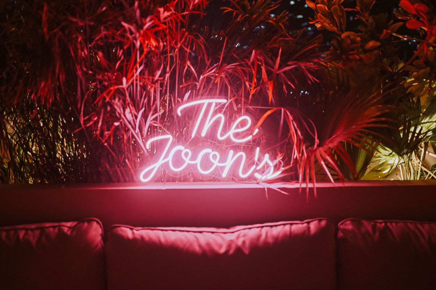 A red neon sign reading 'The Loons' against a dark background with foliage.