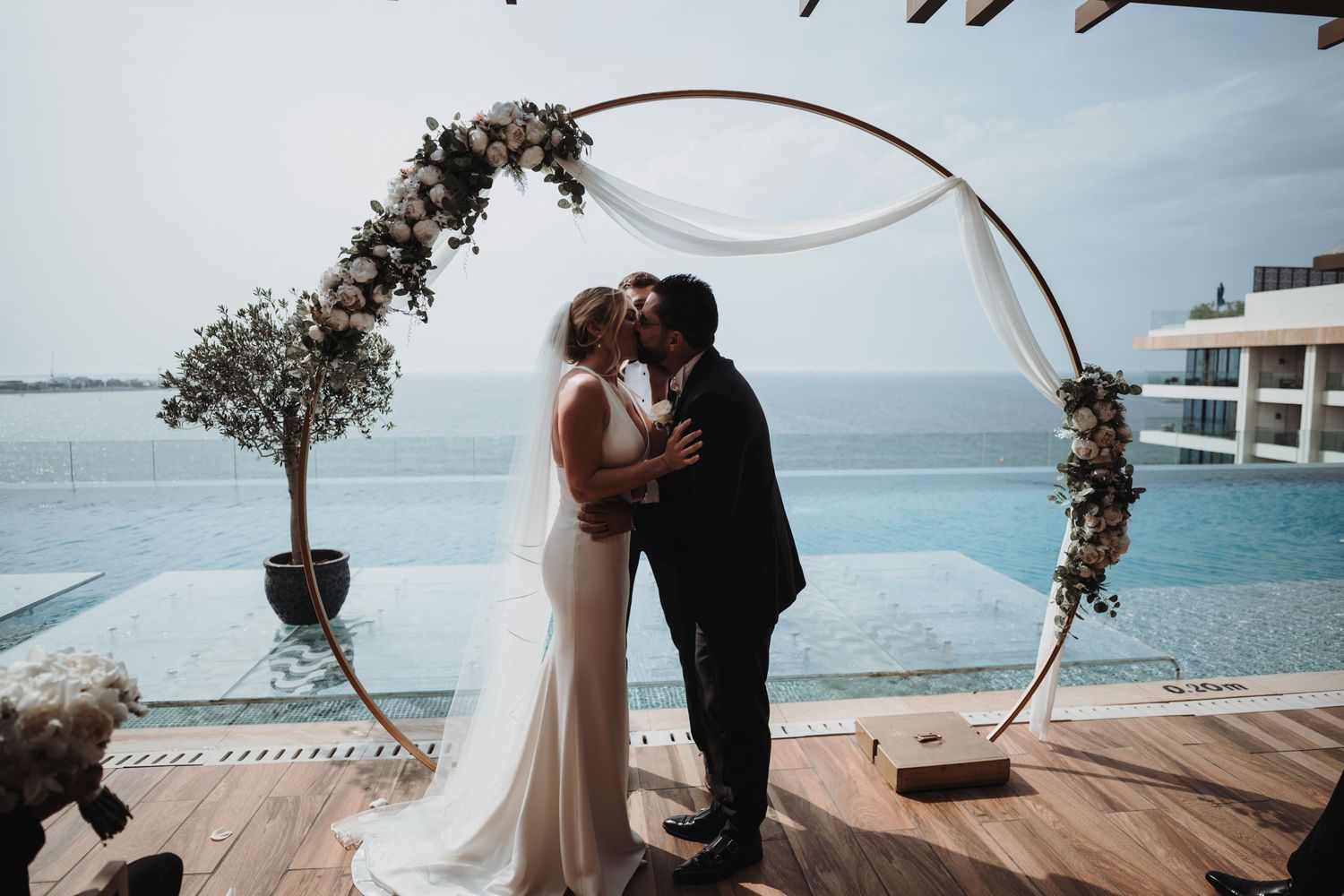 A wedding ceremony in progress on a wooden deck overlooking turquoise waters.