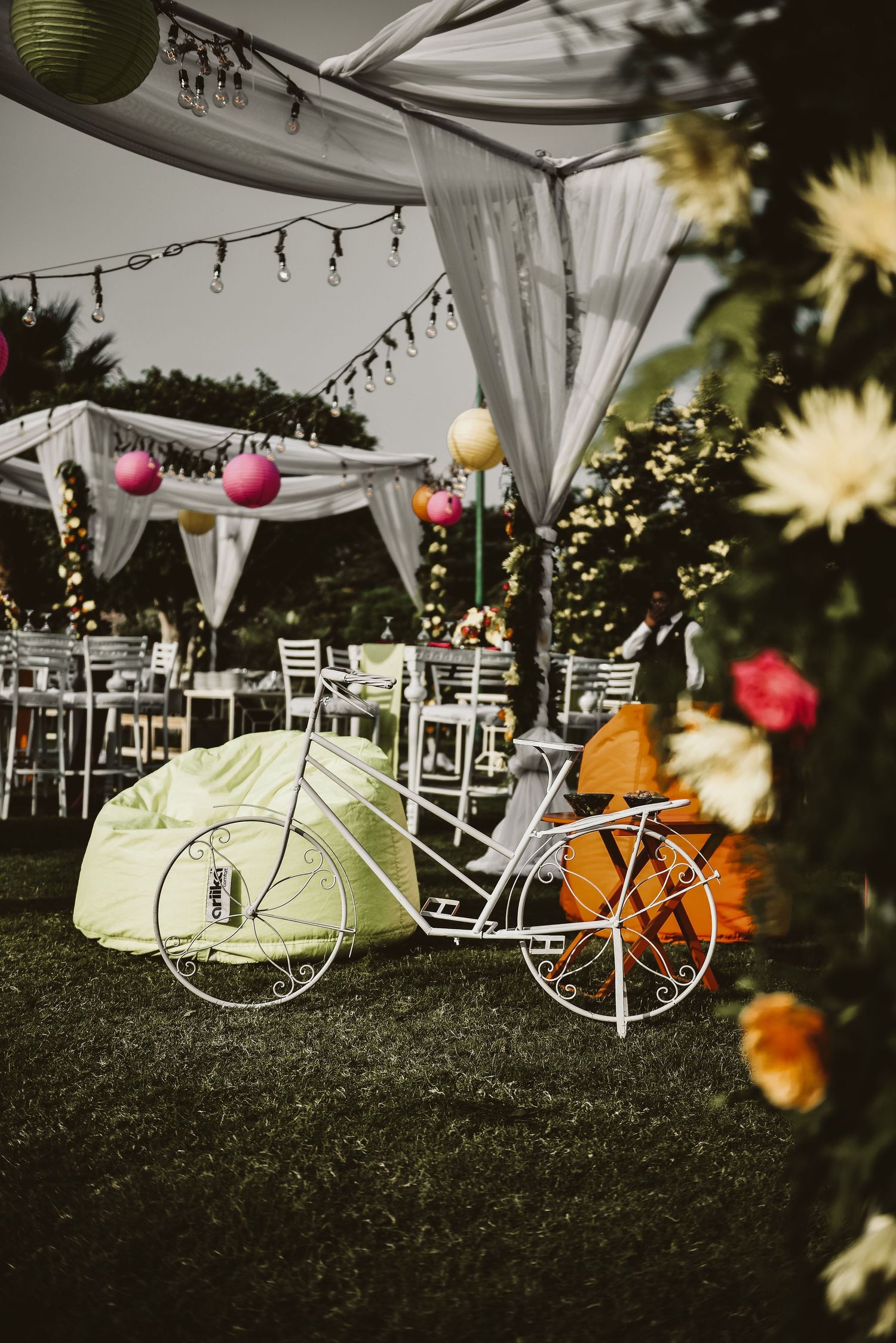 Vintage white bicycles decorated with lanterns and flowers under outdoor wedding tent.