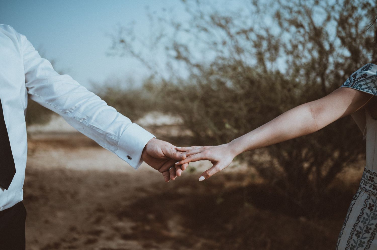 A couple holds hands tenderly in a desert landscape during golden hour.