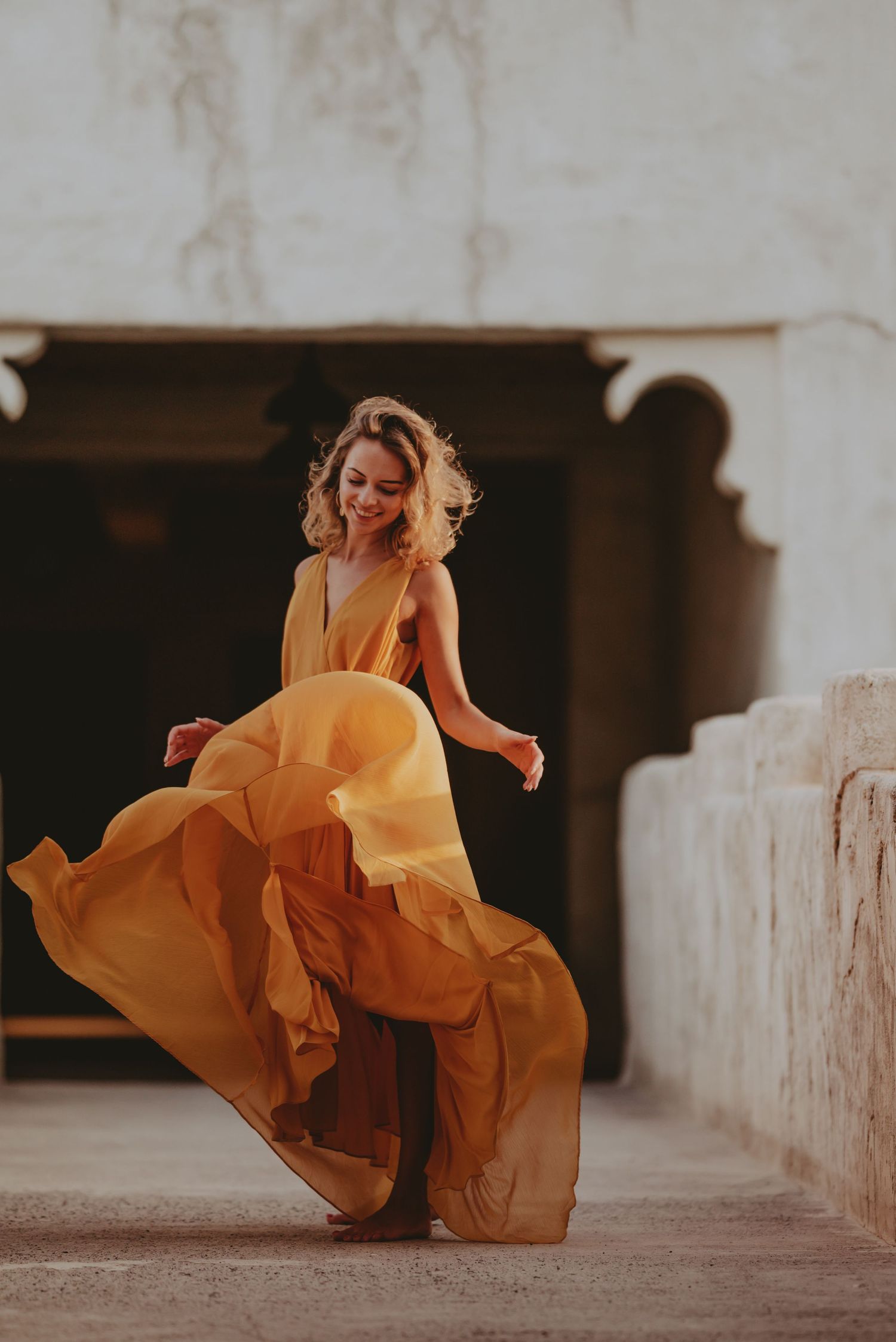 A billowing golden dress catches air in dynamic motion against light stone walls.