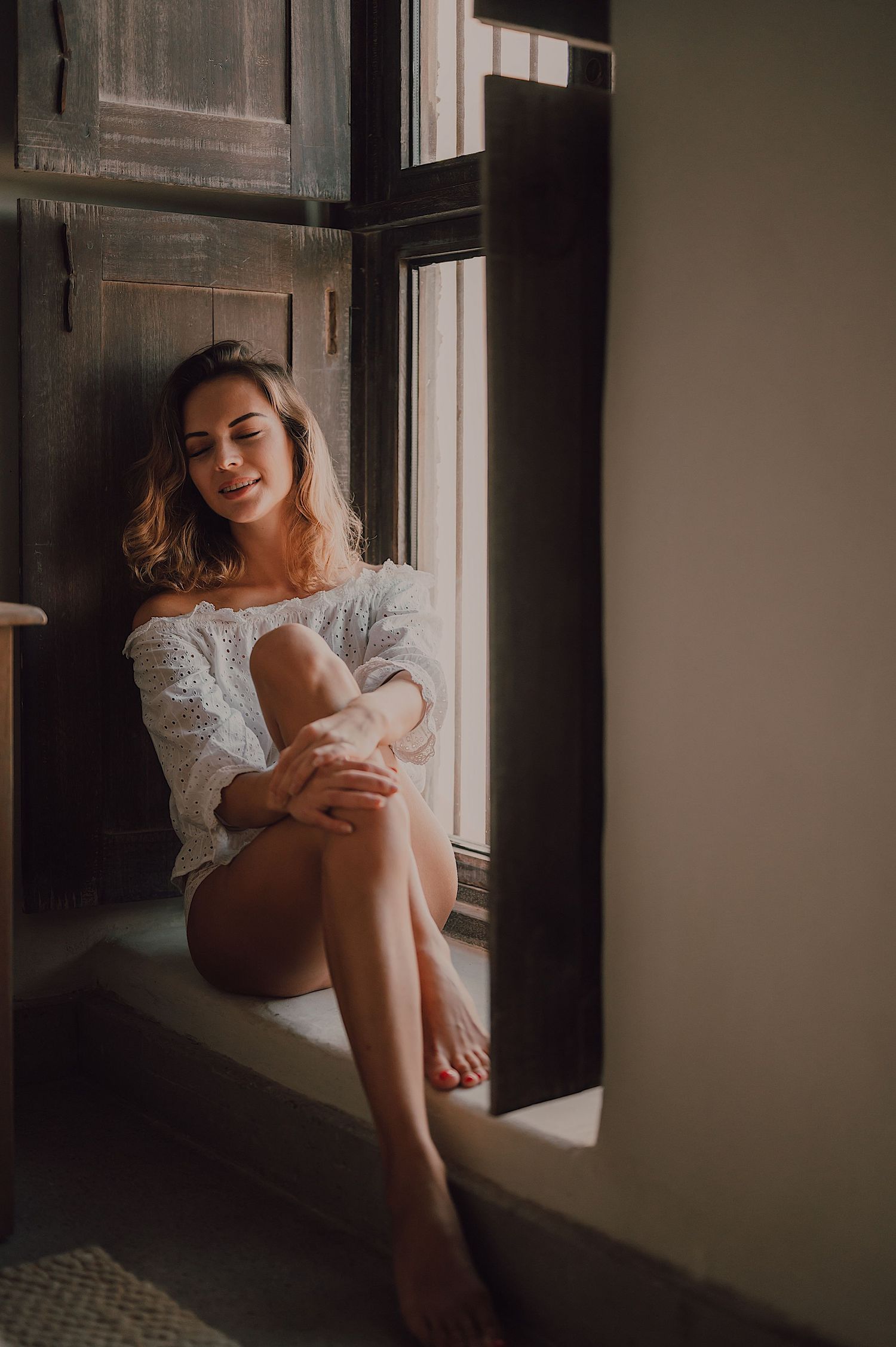 Natural light portrait session by a vintage window with soft shadows.