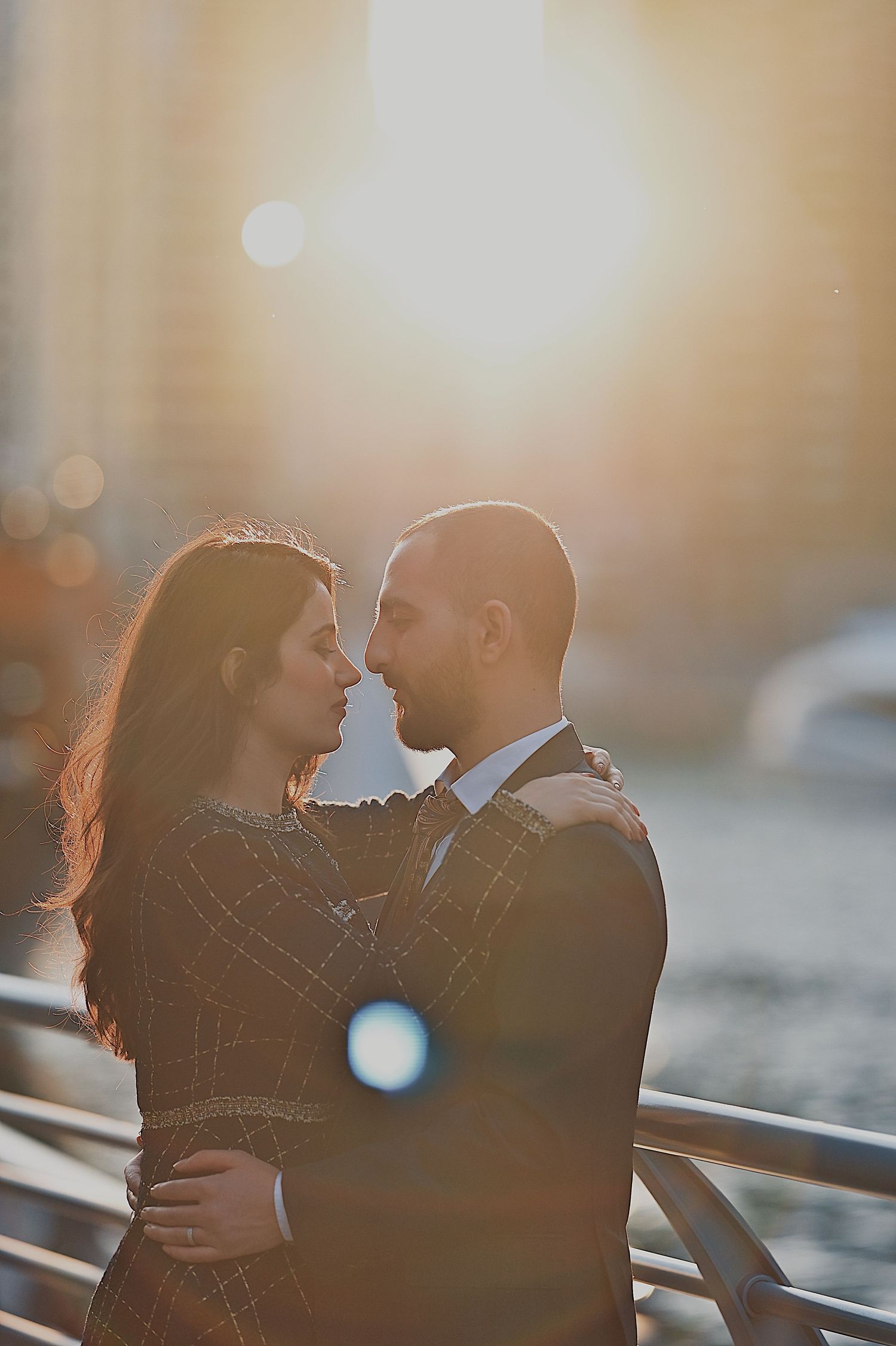 Intimate portrait of couple in warm sunlight against urban backdrop.