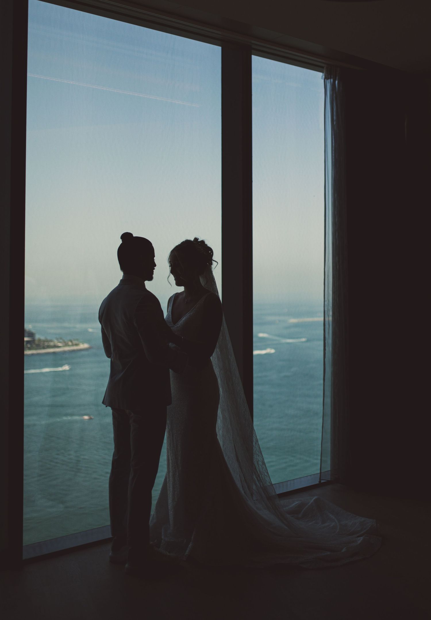 Silhouettes of people standing by large windows overlooking the ocean.