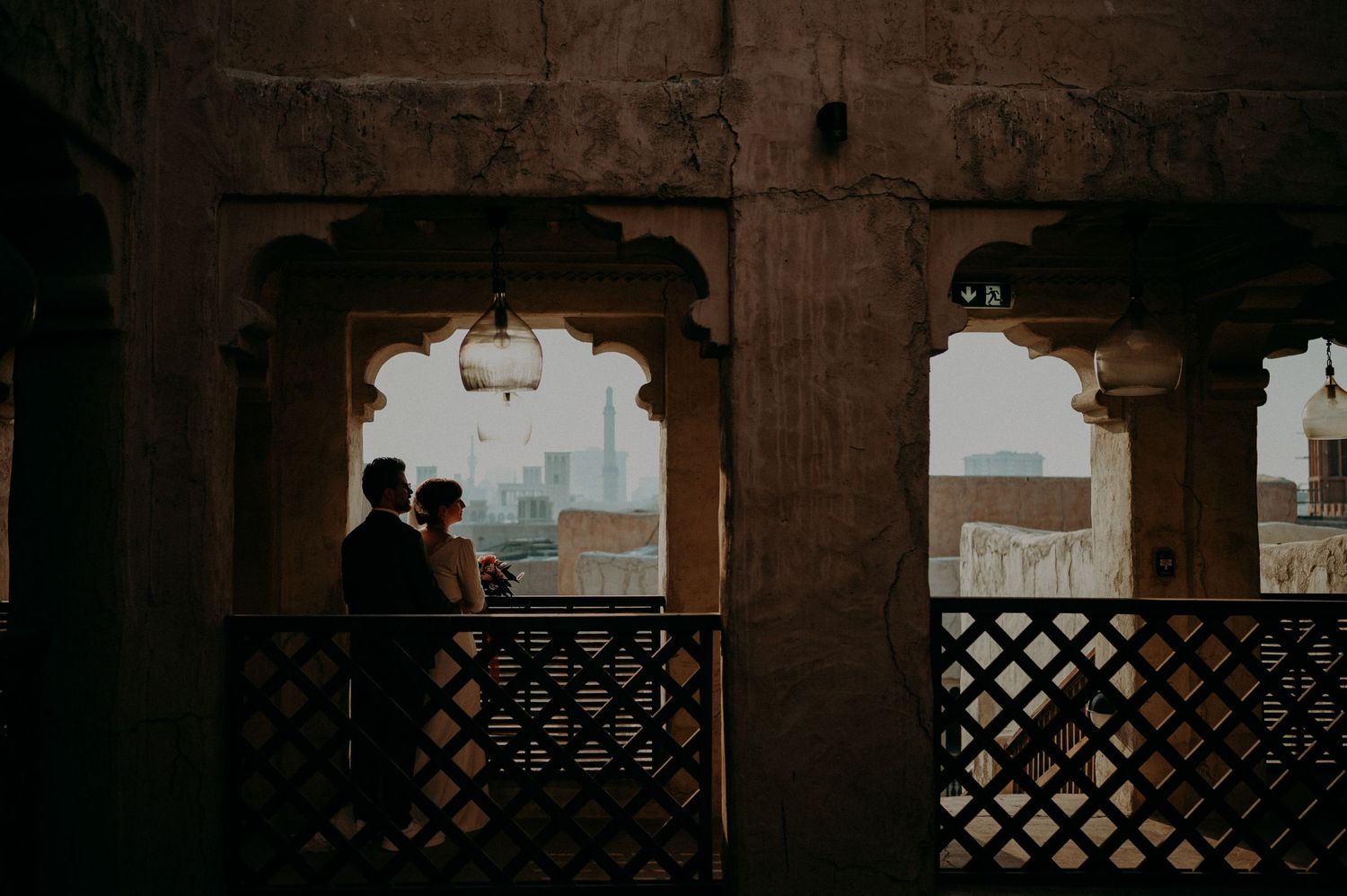 Couple in silhouette standing beneath arched stone columns in a historic building.