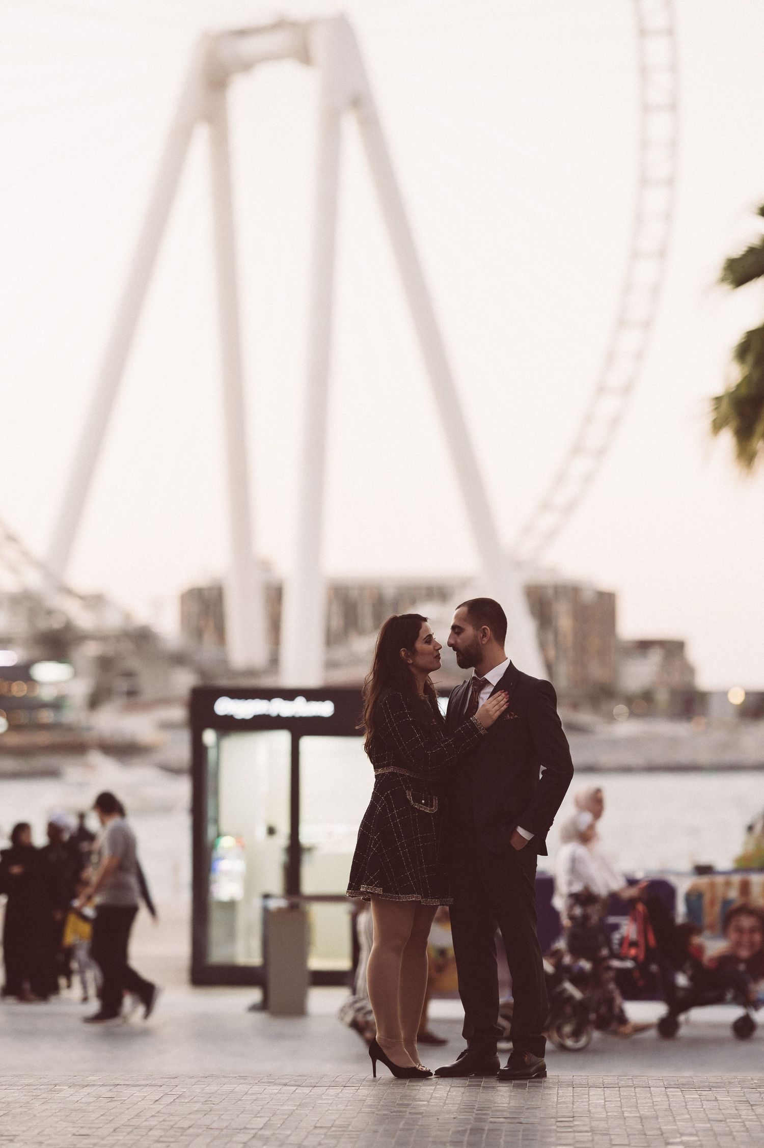 Couple sharing romantic moment with Dubai Wheel silhouette in background.