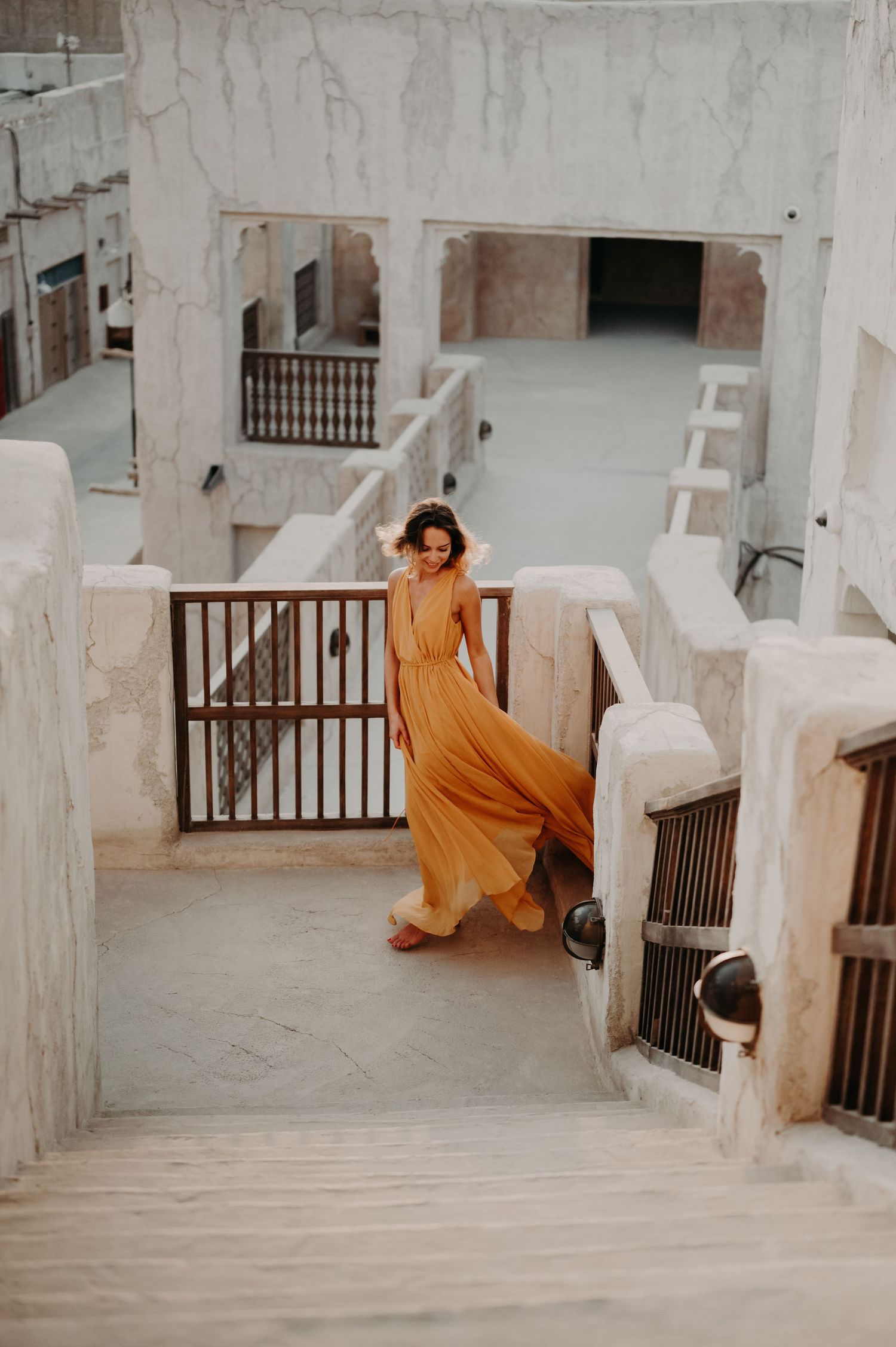 A figure in a flowing orange dress moves gracefully through a white Mediterranean architectural space.