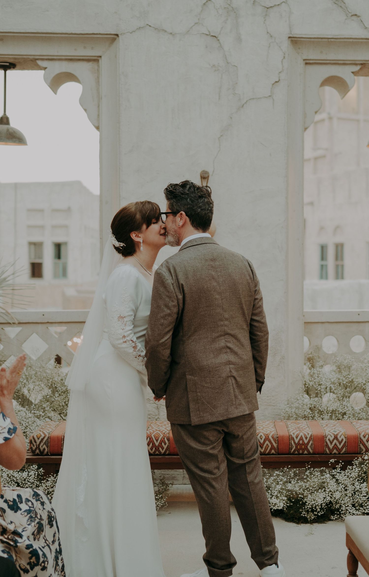 A couple shares an intimate moment against a white stucco wall with decorative plantings.