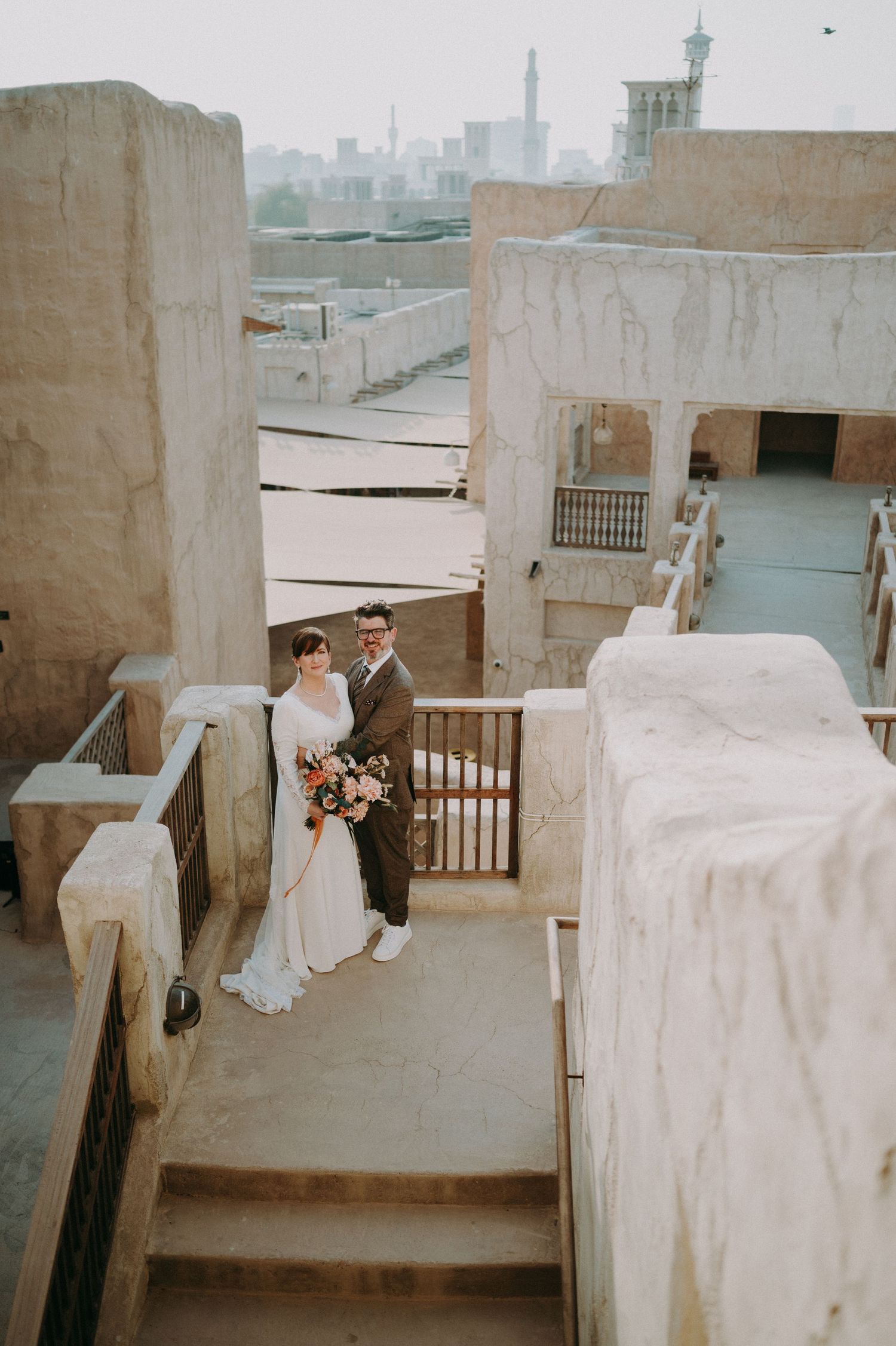 Romantic wedding scene on white stone terrace with city skyline visible in background.