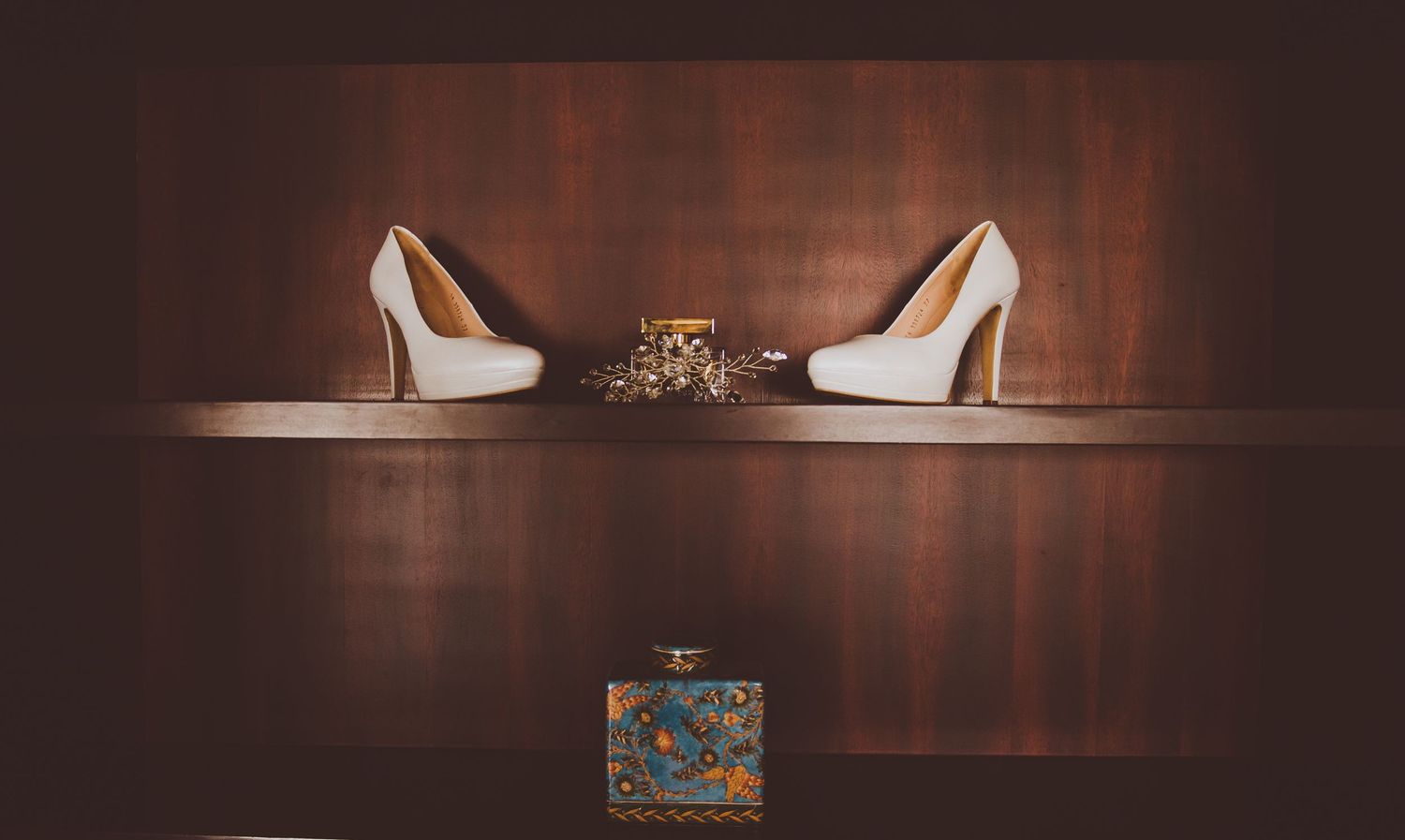 Wedding accessories including white bridal shoes arranged on dark wooden surface.