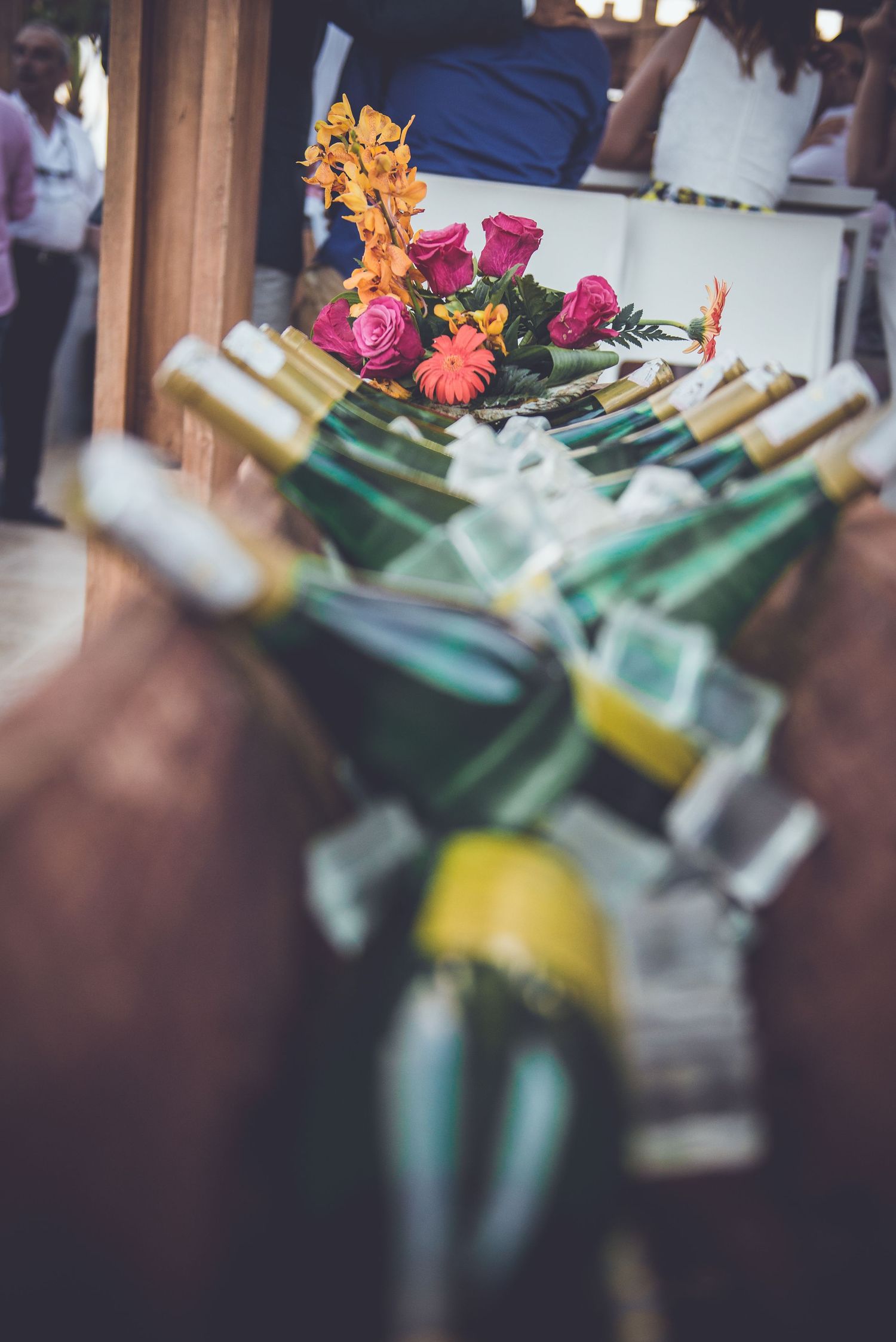 Wedding wine bottles decorated with pink roses and orange flowers arranged in a row.