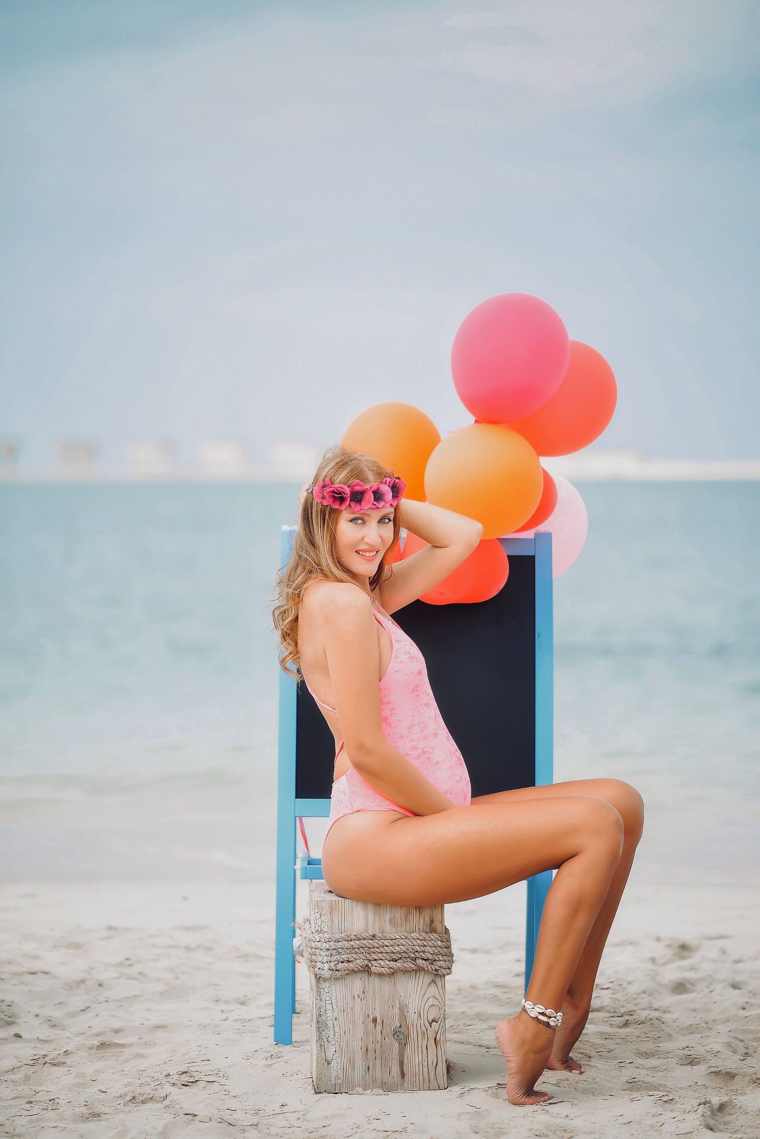 Beach photoshoot with colorful balloons and blue chair on sandy shore.