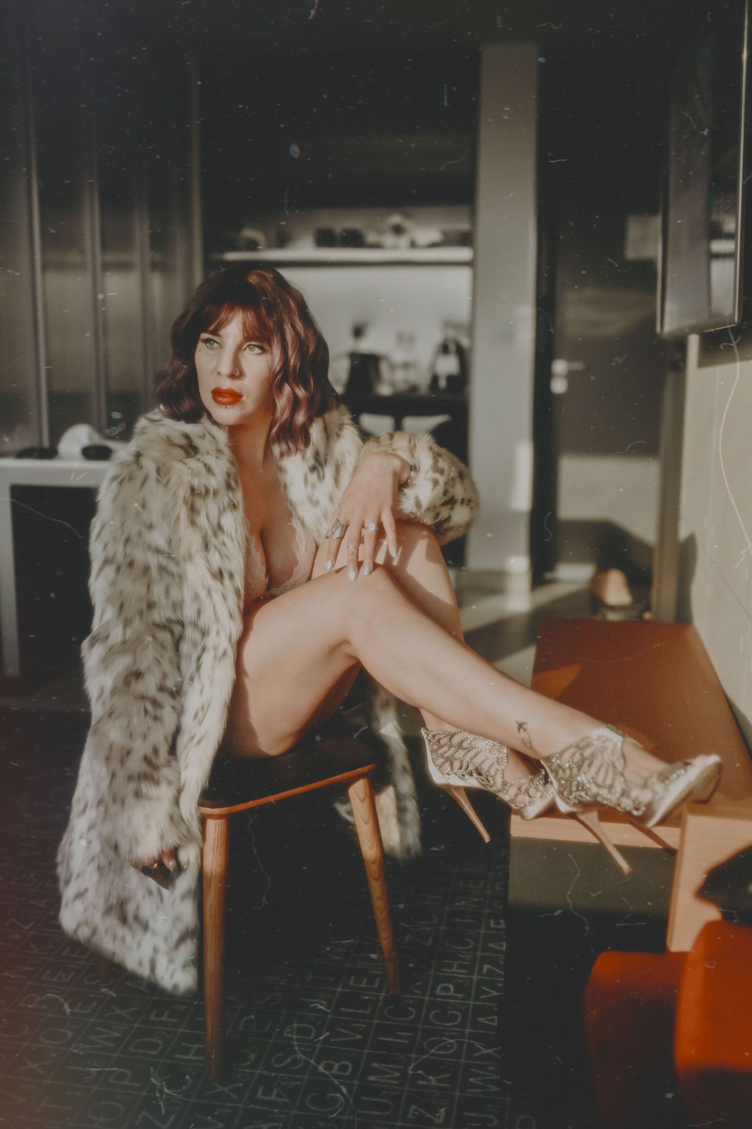 Artistic boudoir photo featuring fur coat and chair in moody lighting.