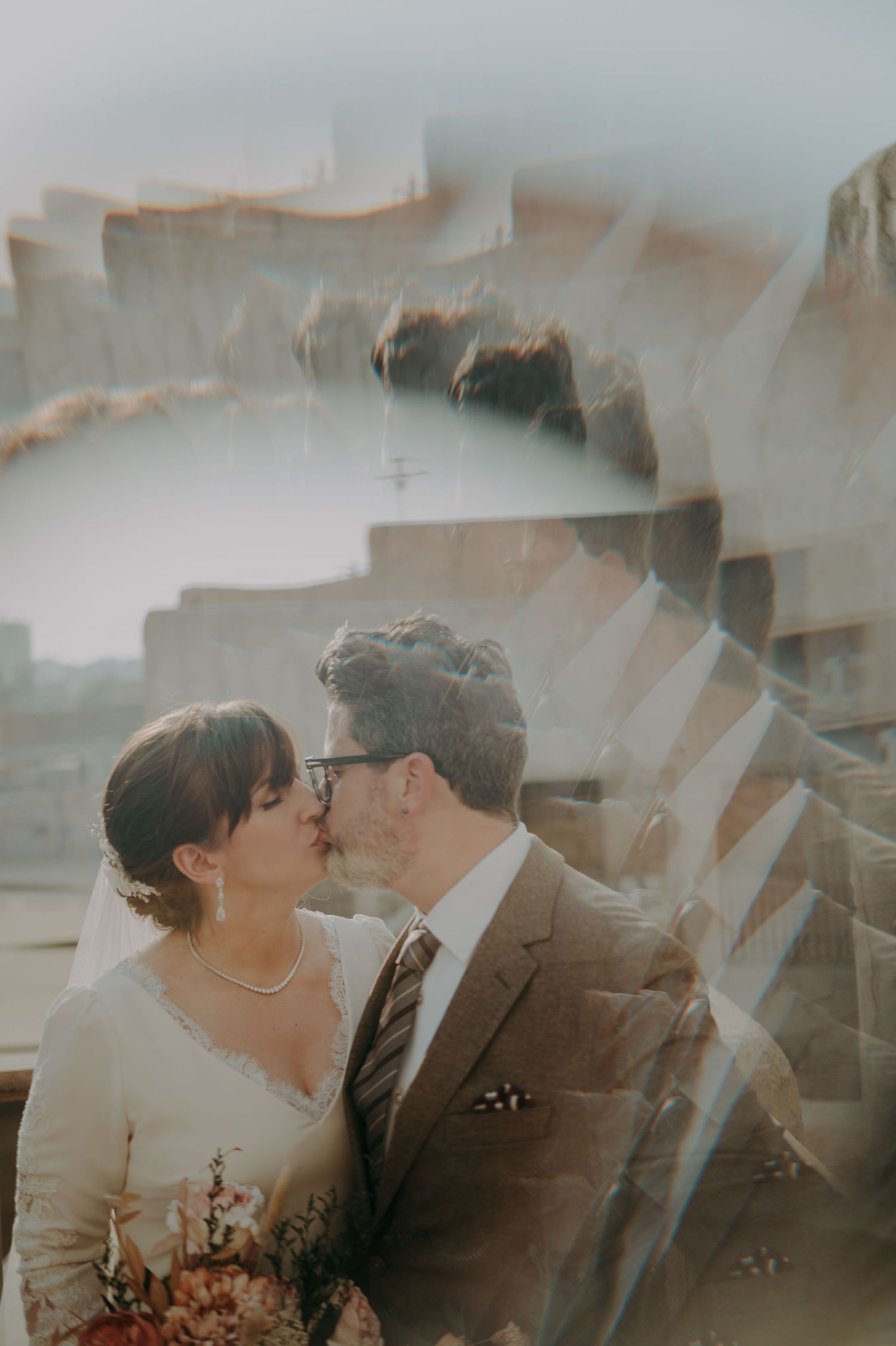 Wedding couple embracing in dreamy sunlit setting with soft muted tones.