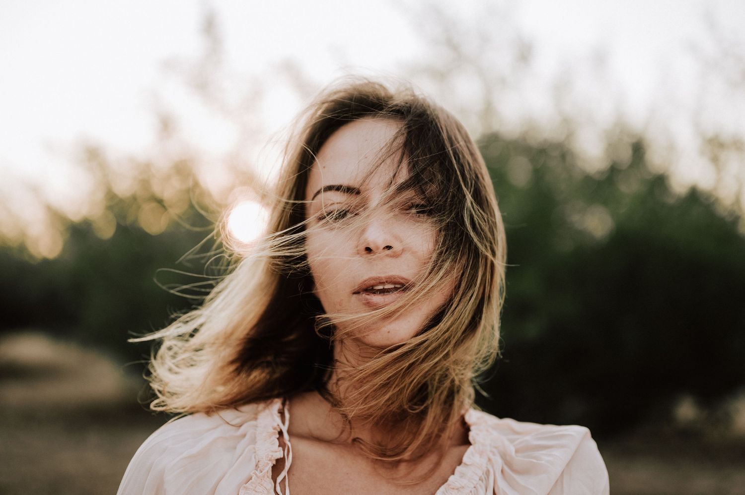 Natural light portrait with wind-tossed hair against a sunset backdrop.