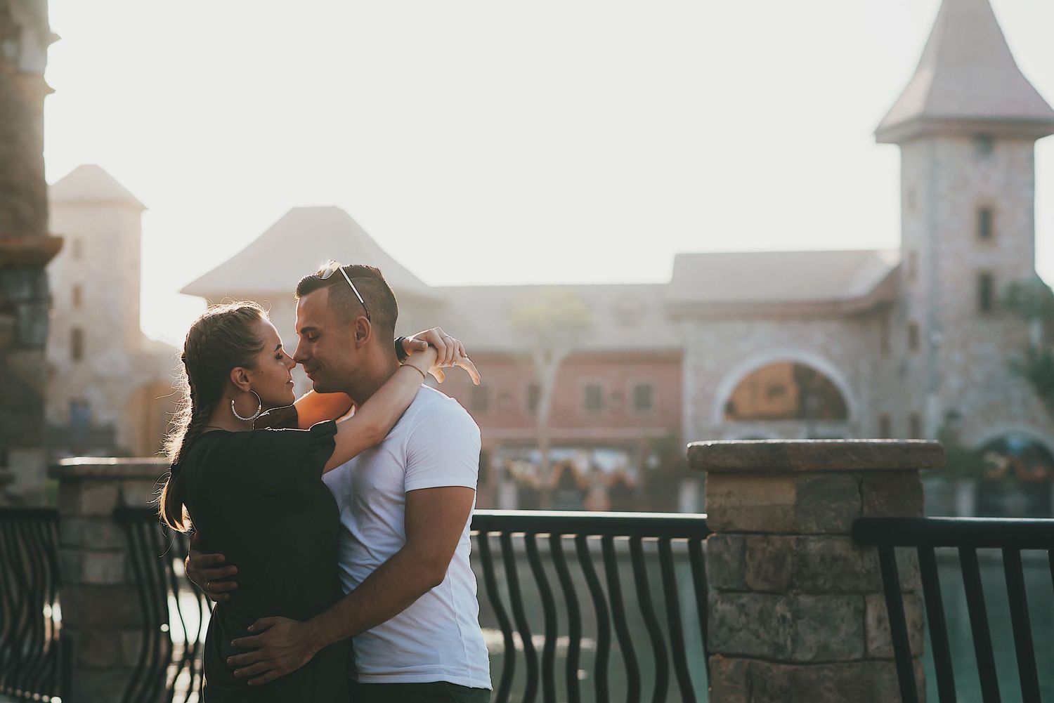 Silhouetted couple embraces against sunset with historic architecture in background.