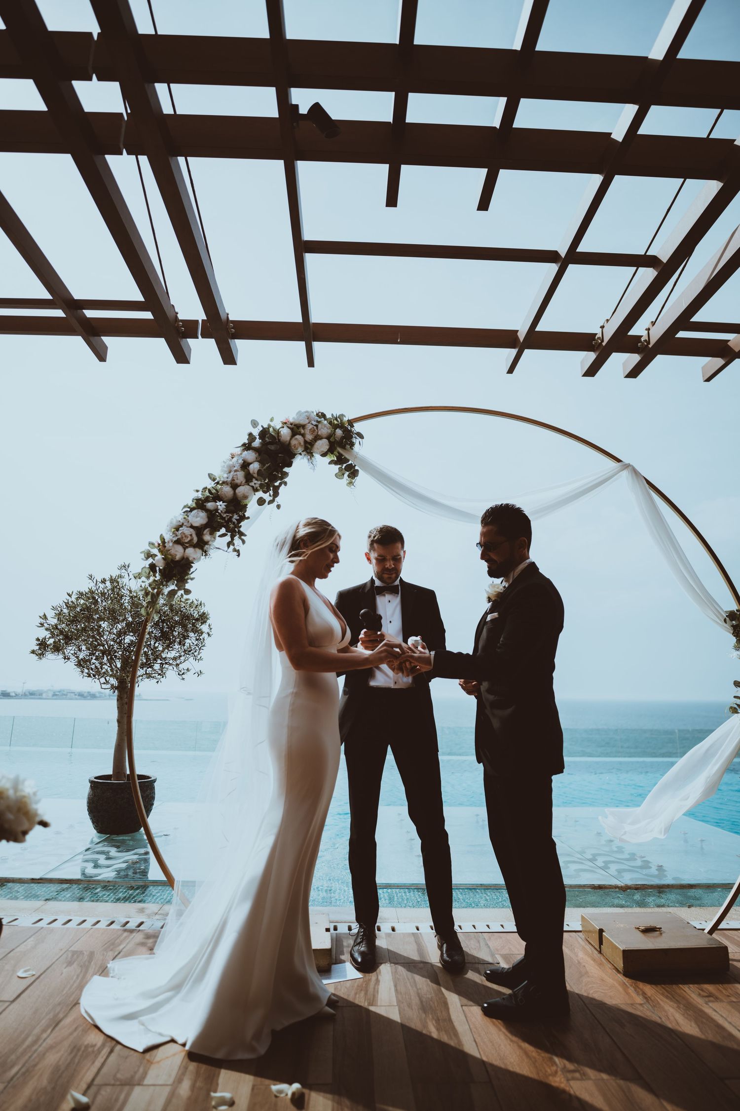 A couple exchanges vows during their oceanfront wedding ceremony under a decorated arch.