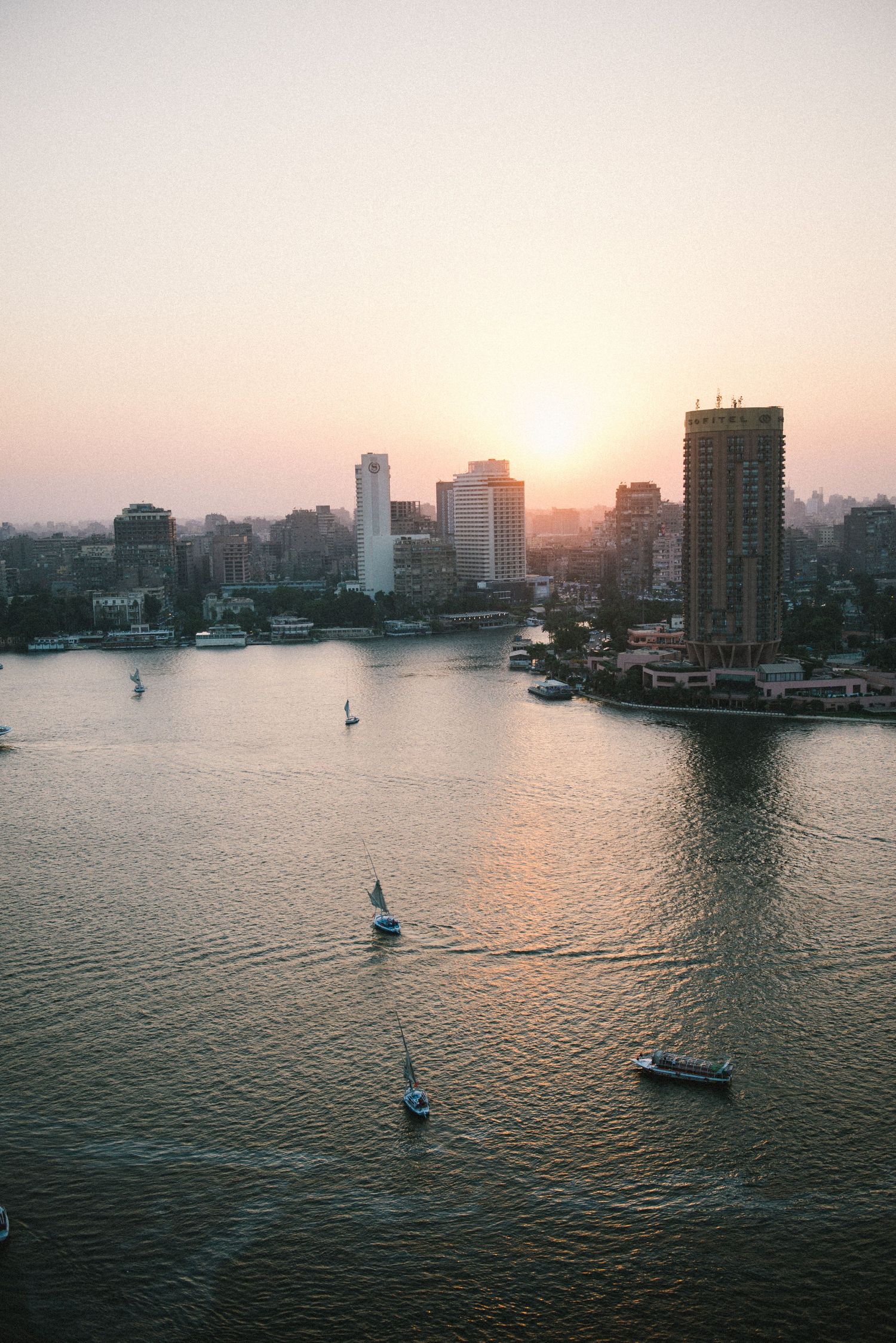 Sunset cityscape view over waterfront with boats sailing across harbor.