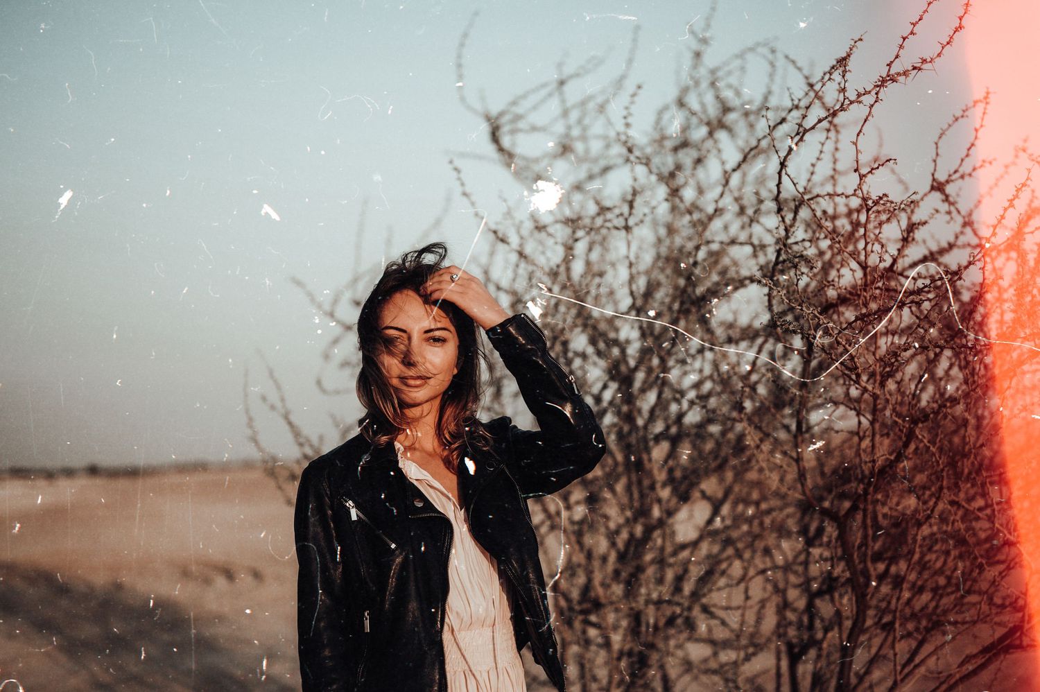 Artistic portrait with dramatic red lighting and shadows against a natural outdoor backdrop.