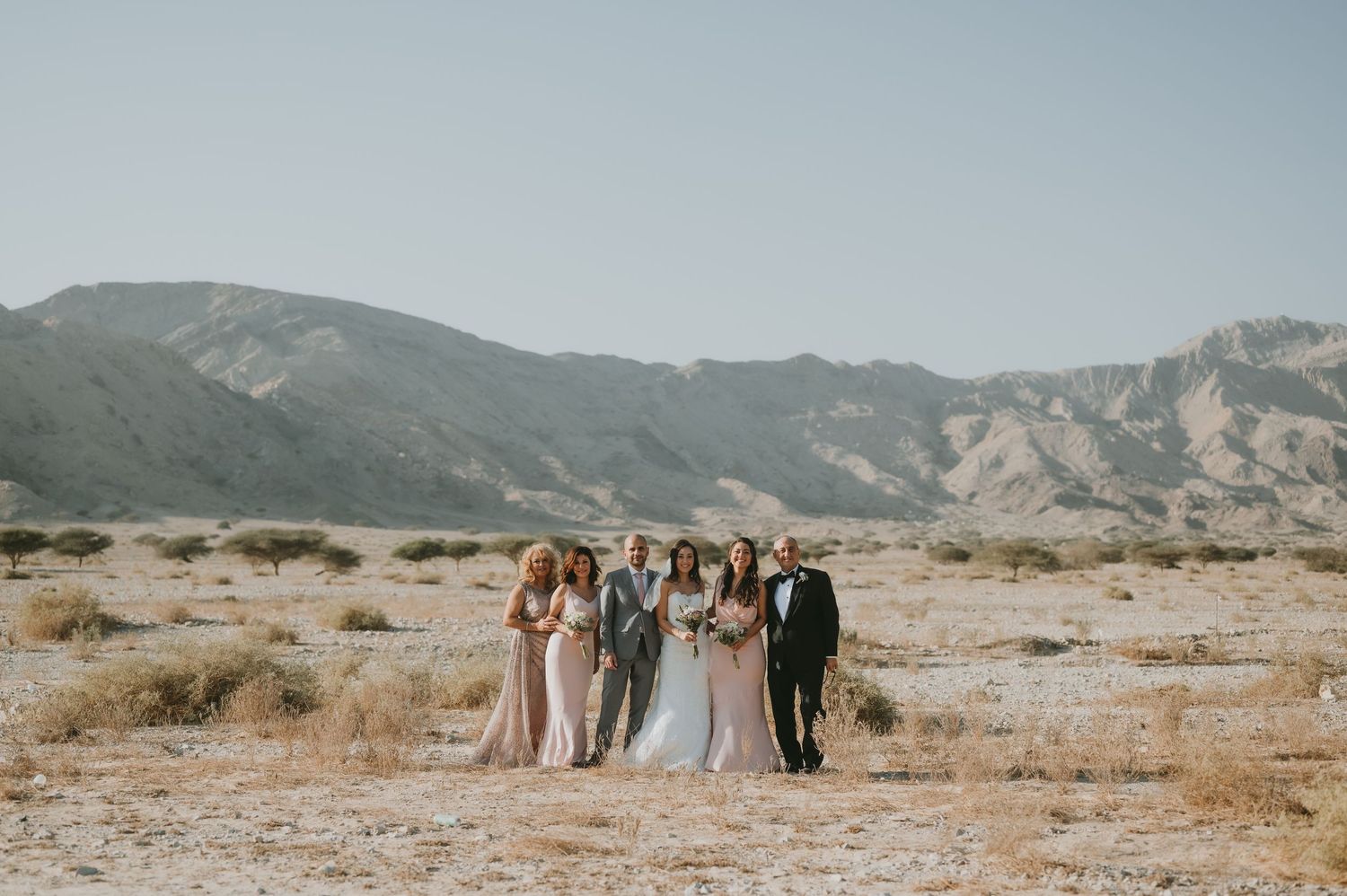 Wedding group stands together in arid desert setting with mountain backdrop.