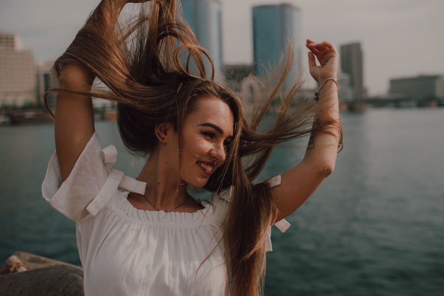 Woman in white dress spins and dances by the waterfront at sunset.