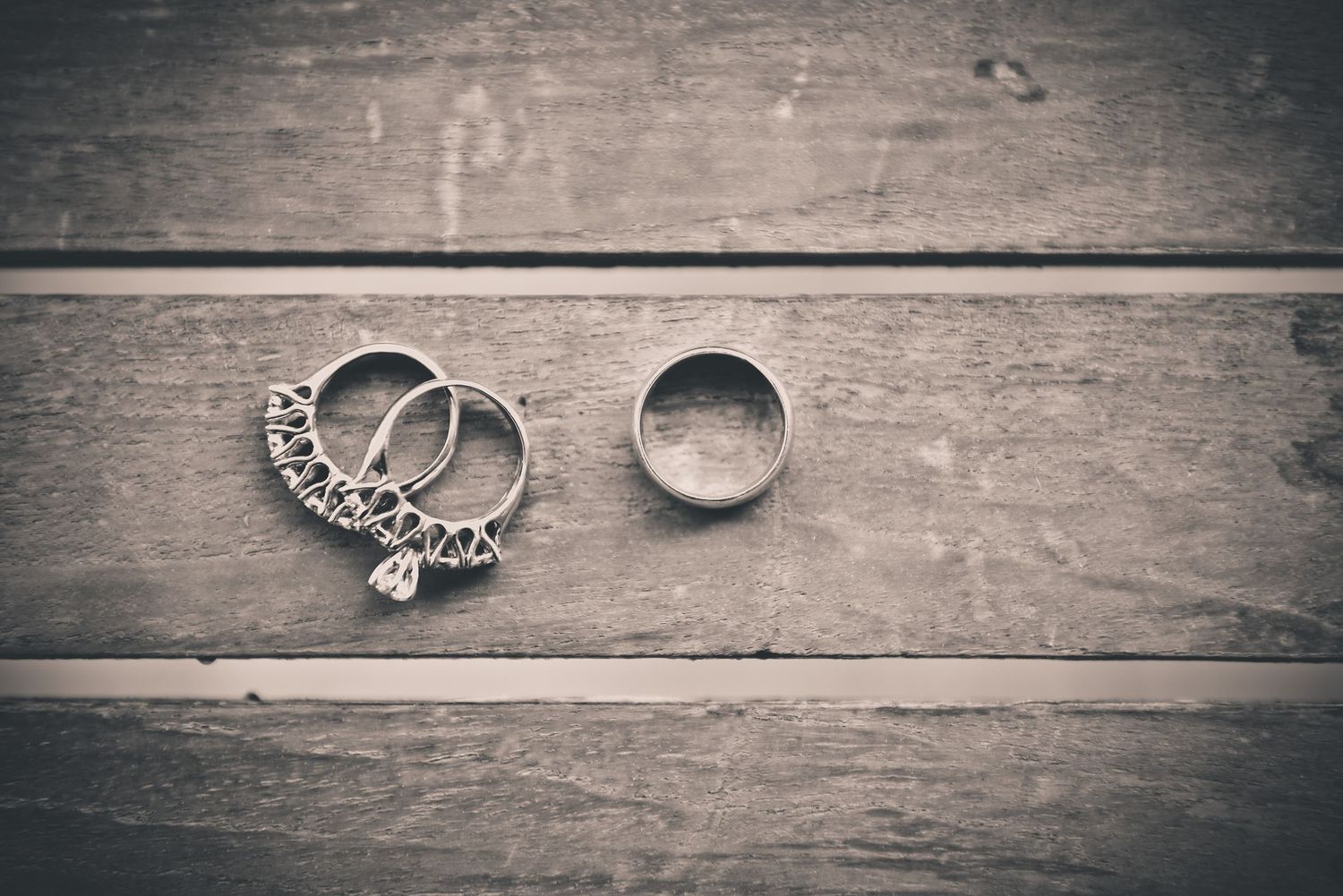Wedding rings and jewelry arranged on rustic wooden planks in vintage style.