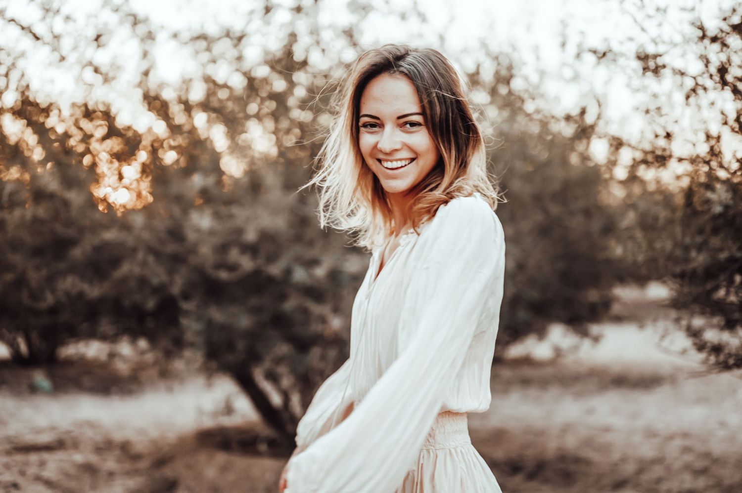 Portrait in a white dress against a warm sunset background with natural outdoor lighting.