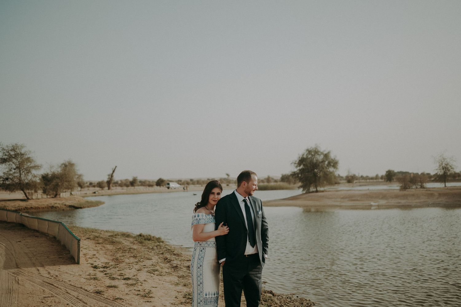Wide landscape shot of couple by lake with desert scenery in background.