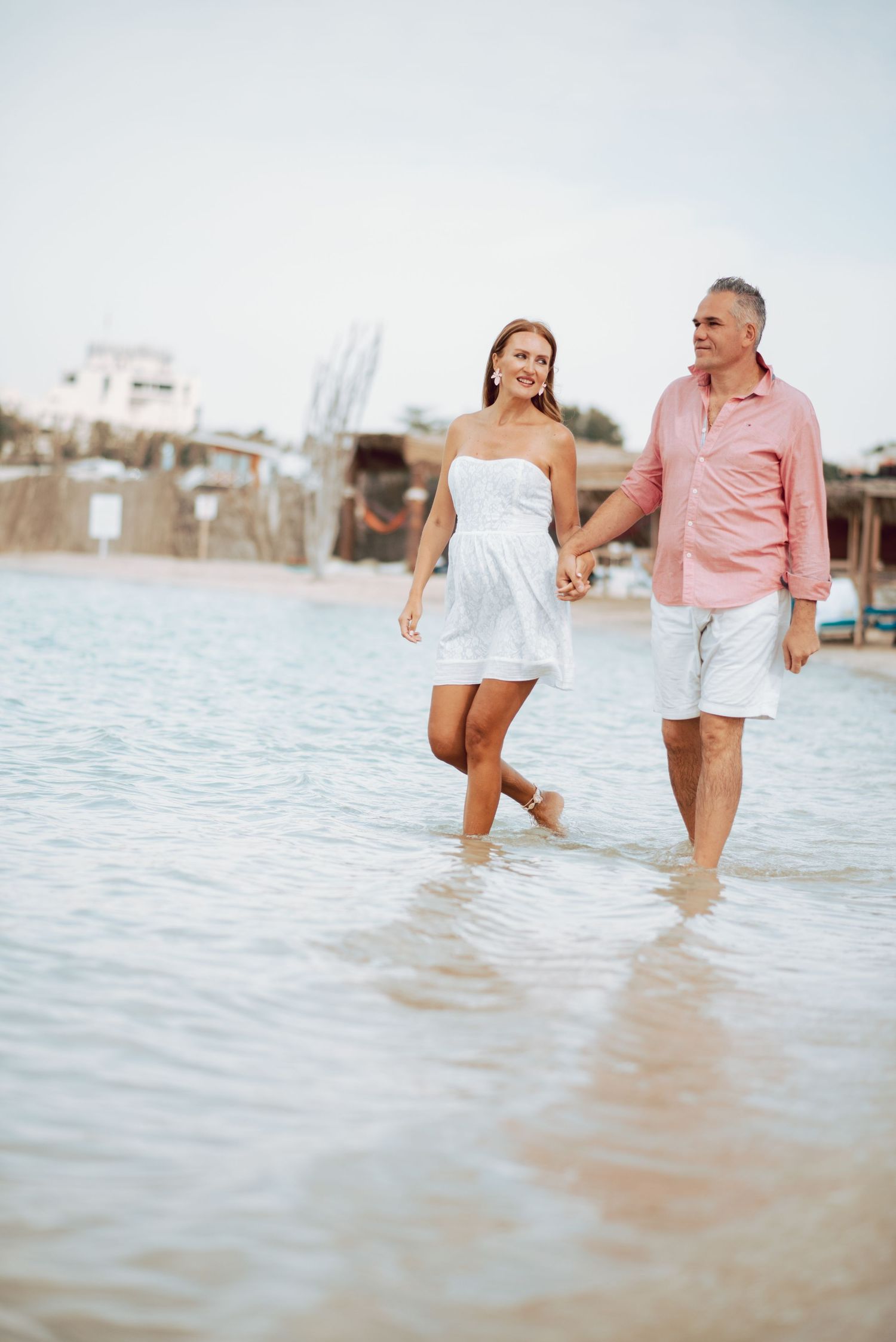 Couple walking and splashing in shallow ocean water during sunset photoshoot.