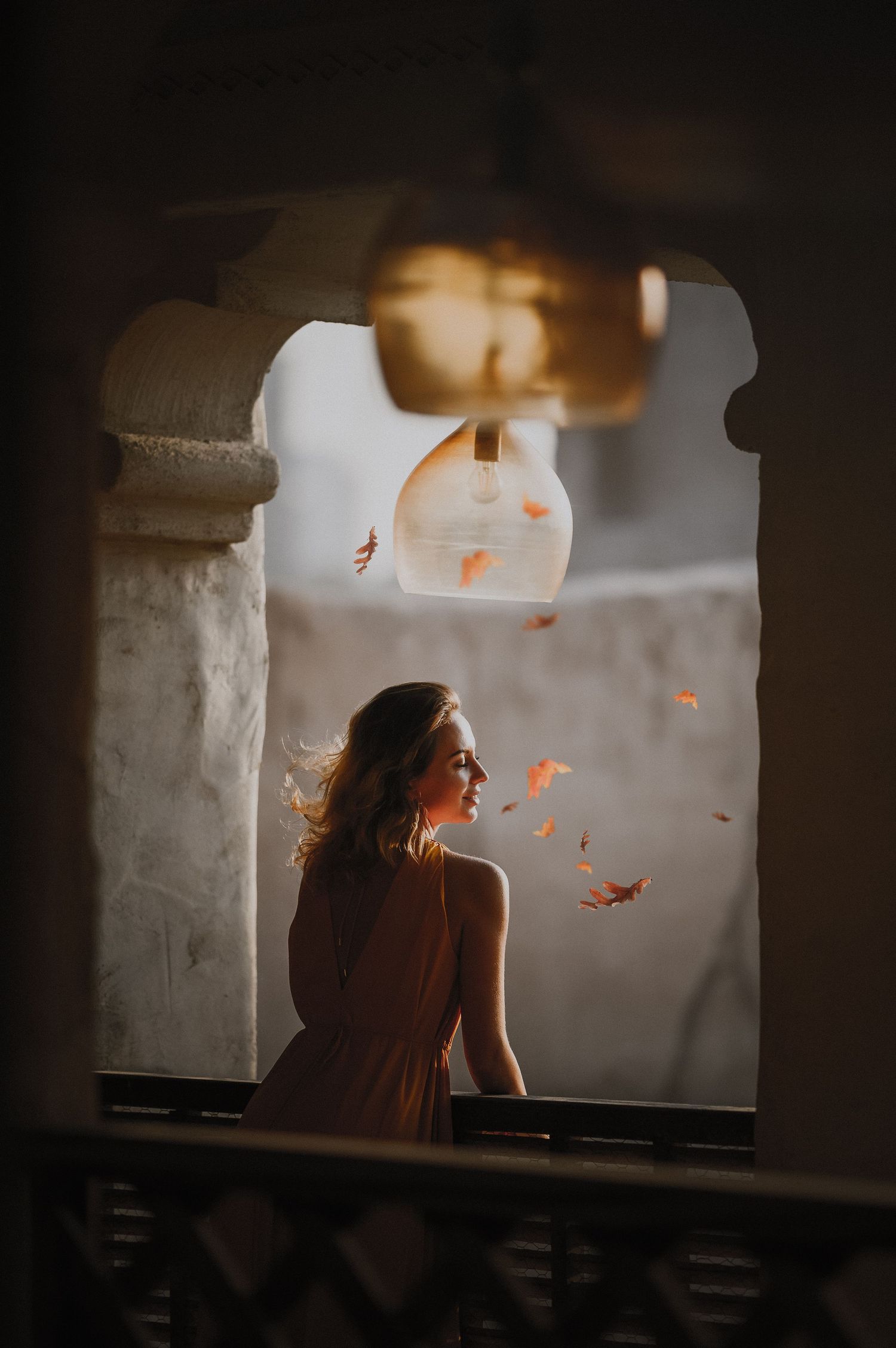 Silhouette through stone archway with floating autumn leaves and dramatic backlighting.