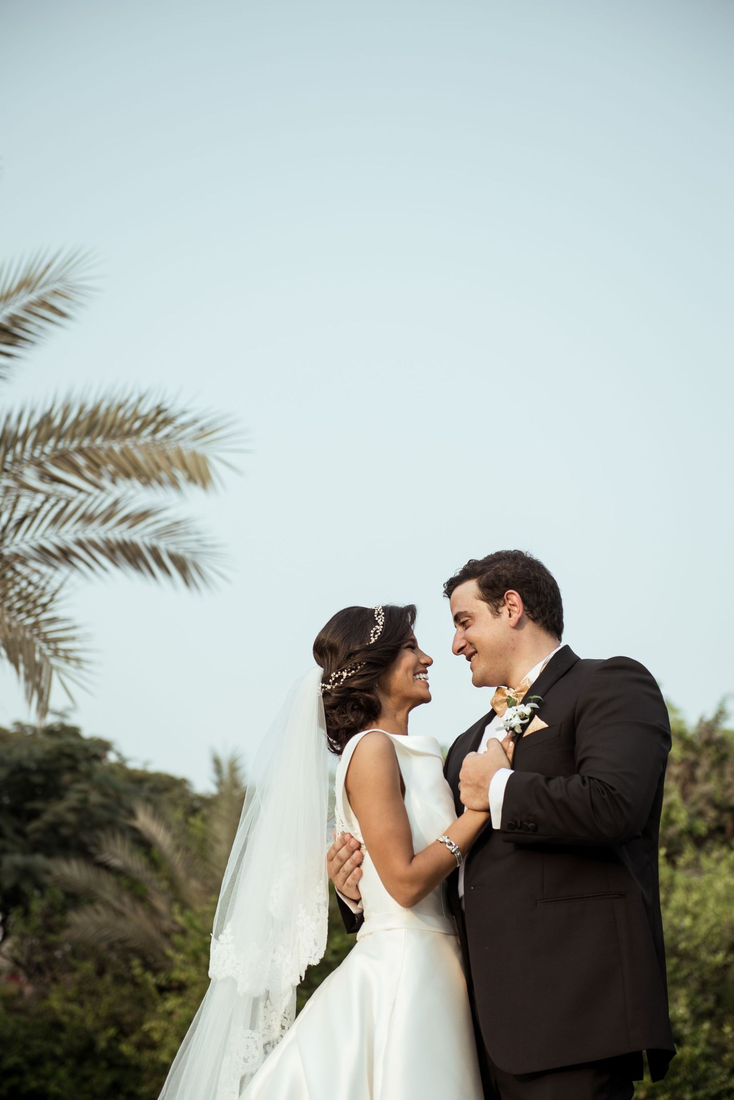 Candid moment of laughter between newlyweds with palm trees in the background.