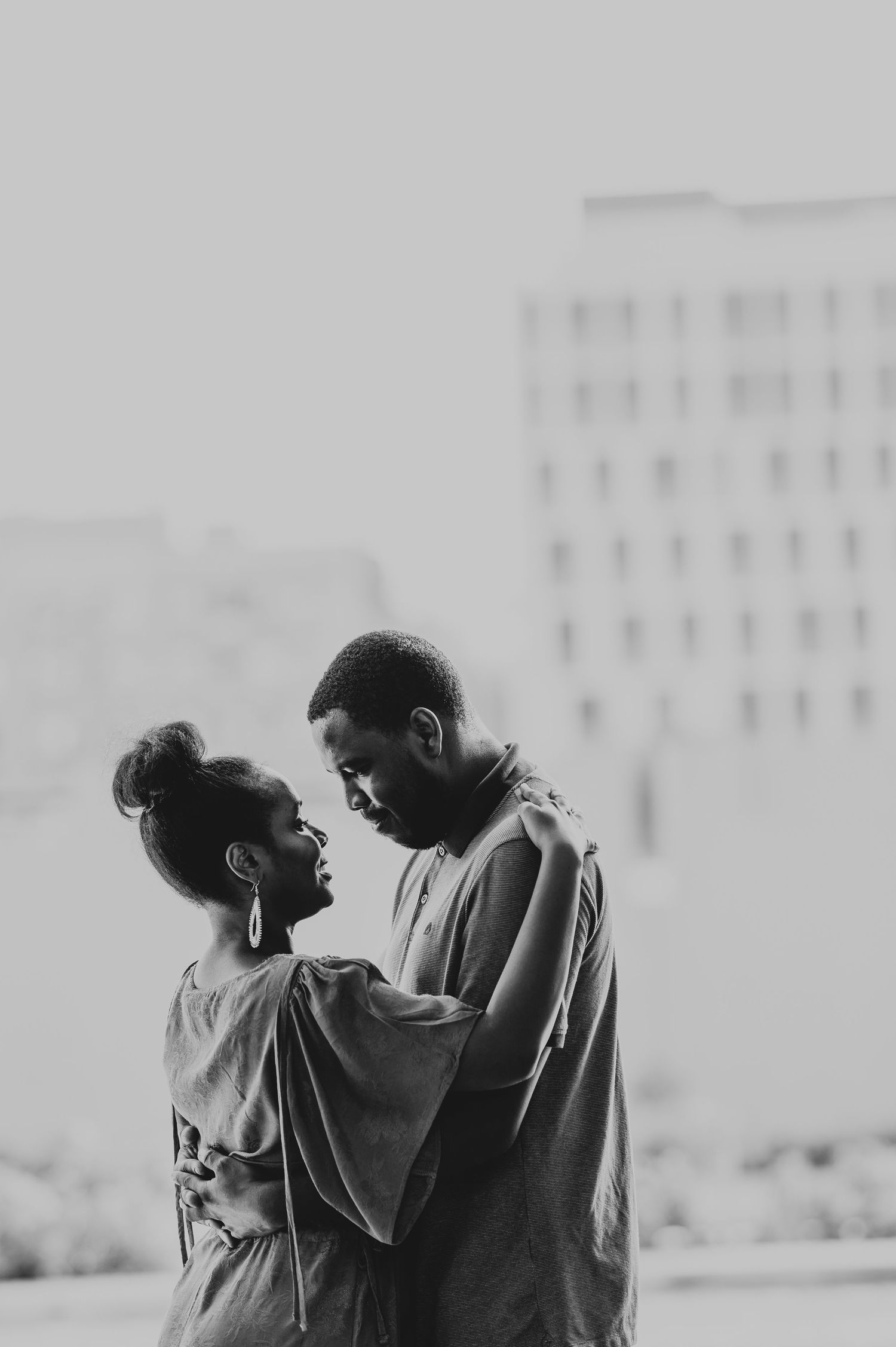 A romantic black and white portrait of a couple sharing an intimate moment against a city backdrop.