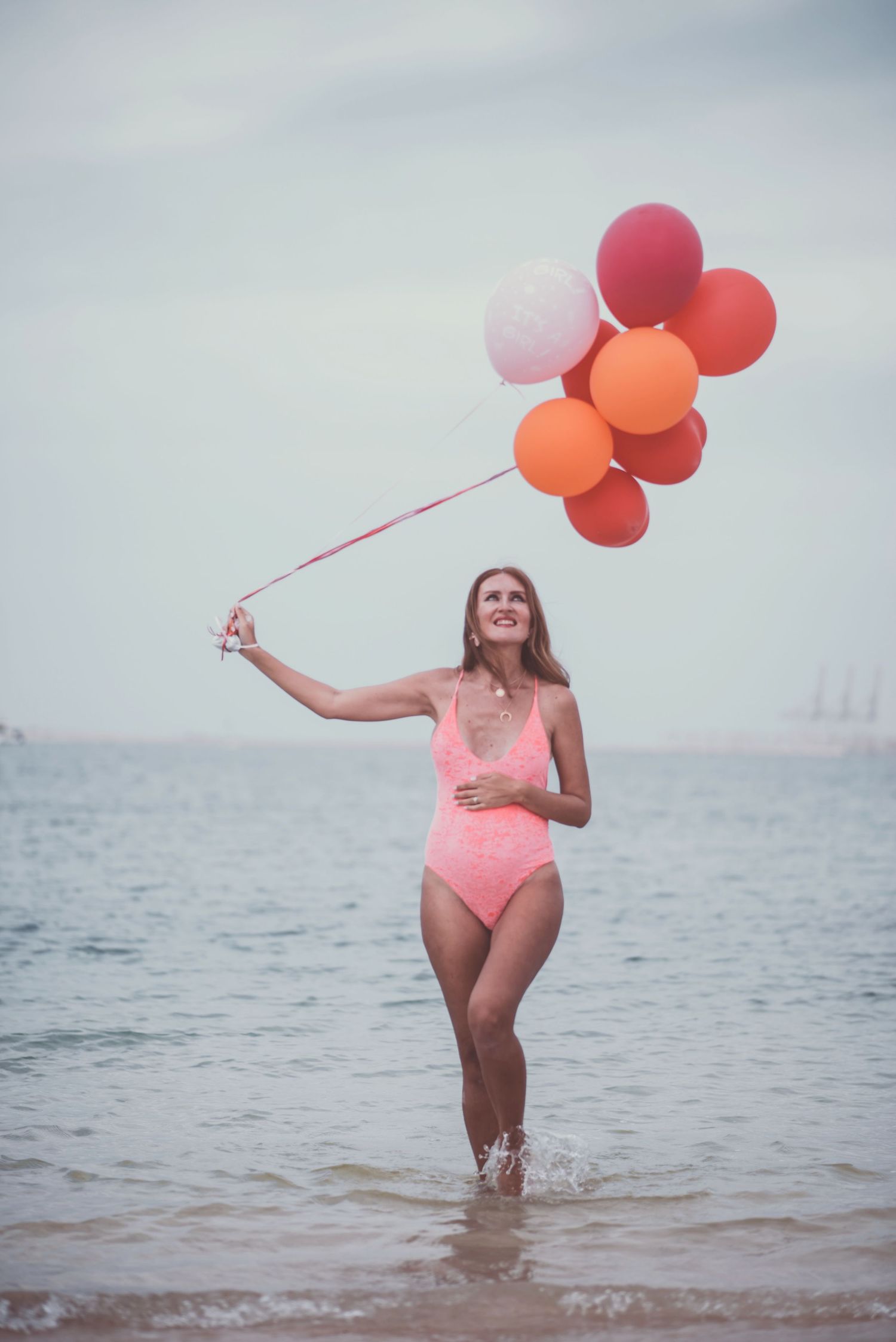 Woman in pink swimsuit plays with colorful balloons while standing in ocean water.