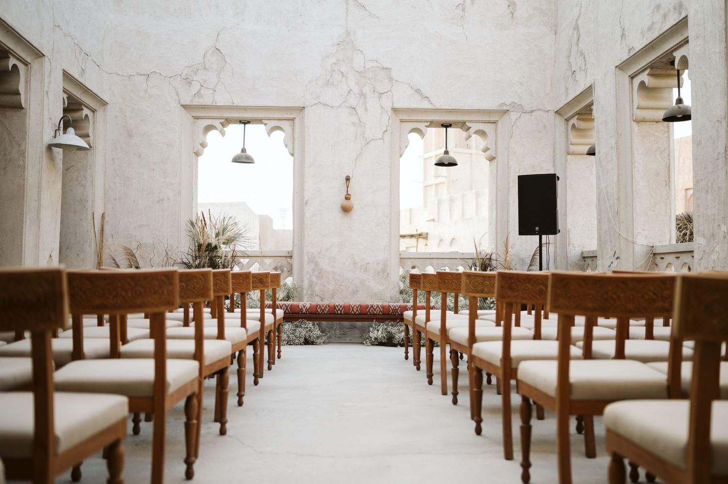 Long rows of wooden pews line a bright white chapel interior with hanging pendant lights.
