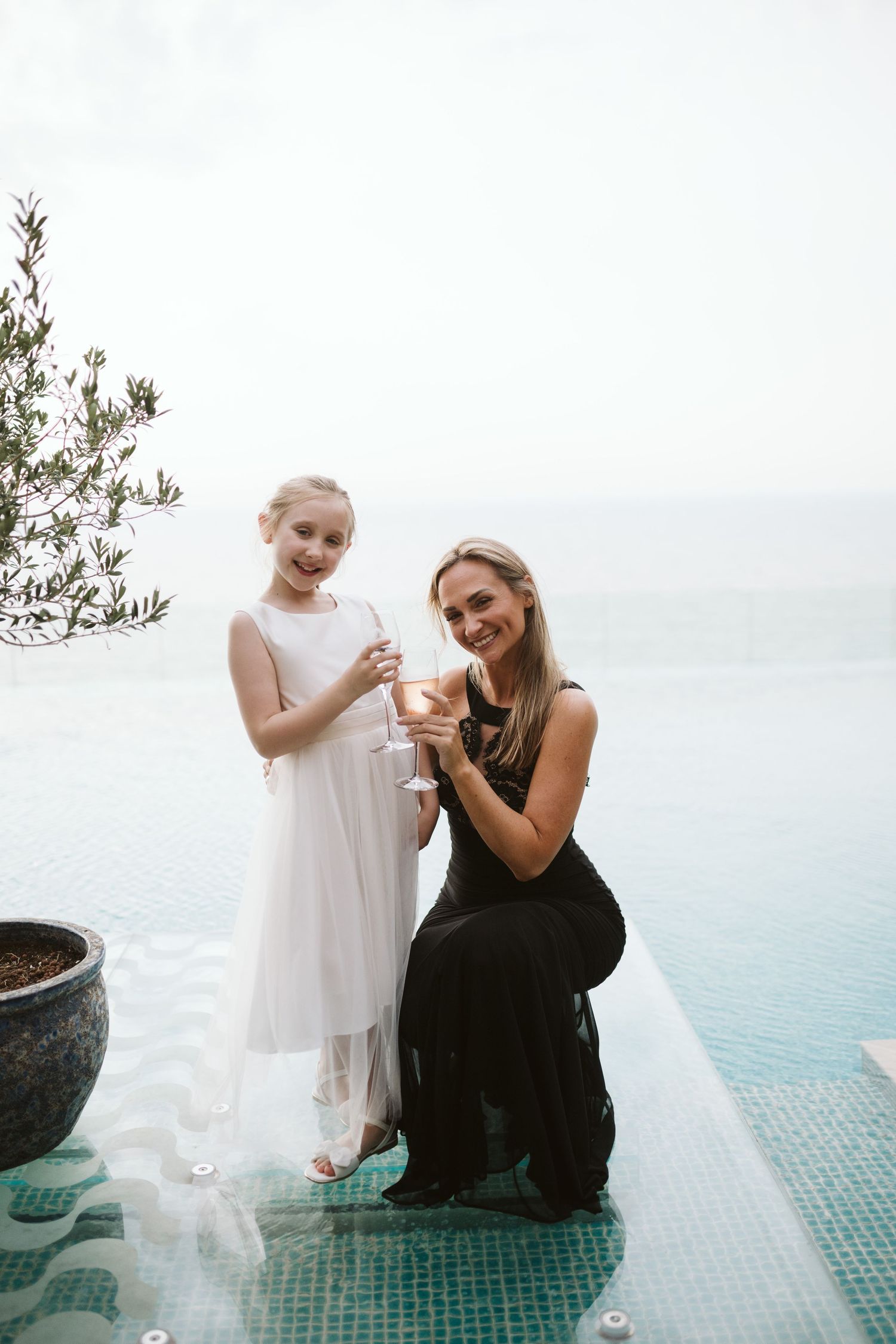 Two figures sitting by a poolside overlooking the ocean.