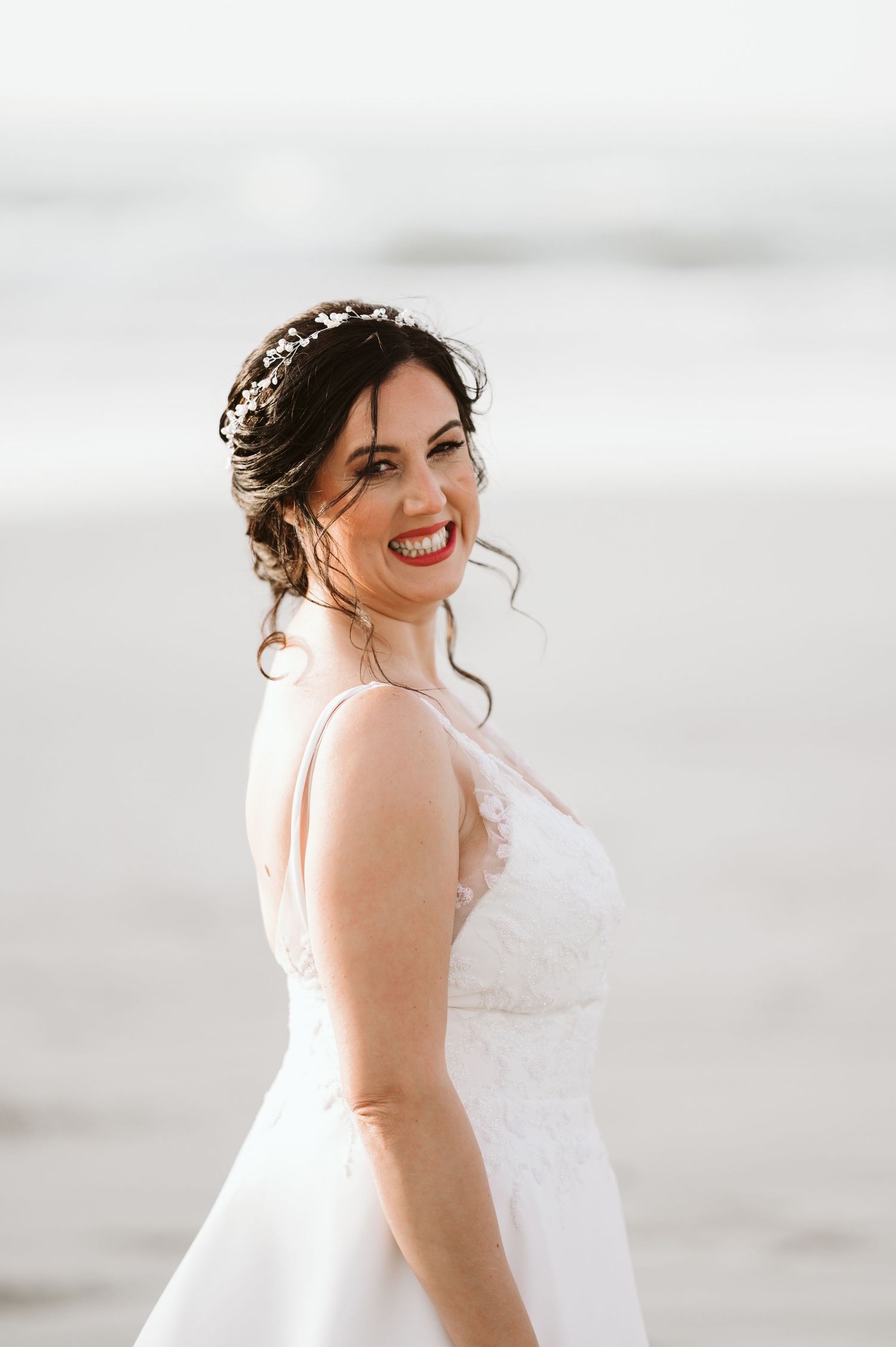 A bride in a white wedding dress poses against a bright background with a radiant smile.