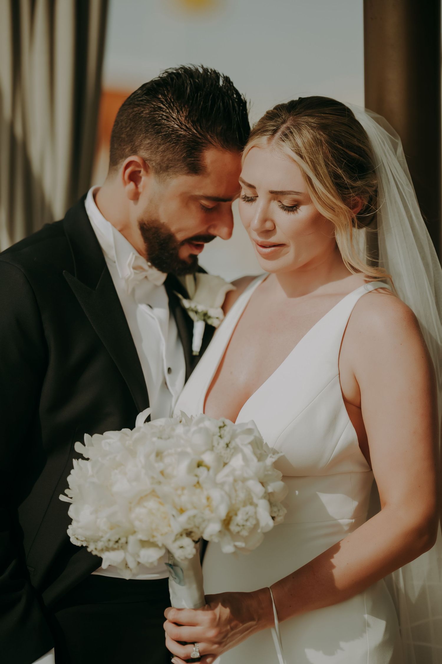 Intimate wedding portrait showing couple holding white floral bouquet in romantic pose.