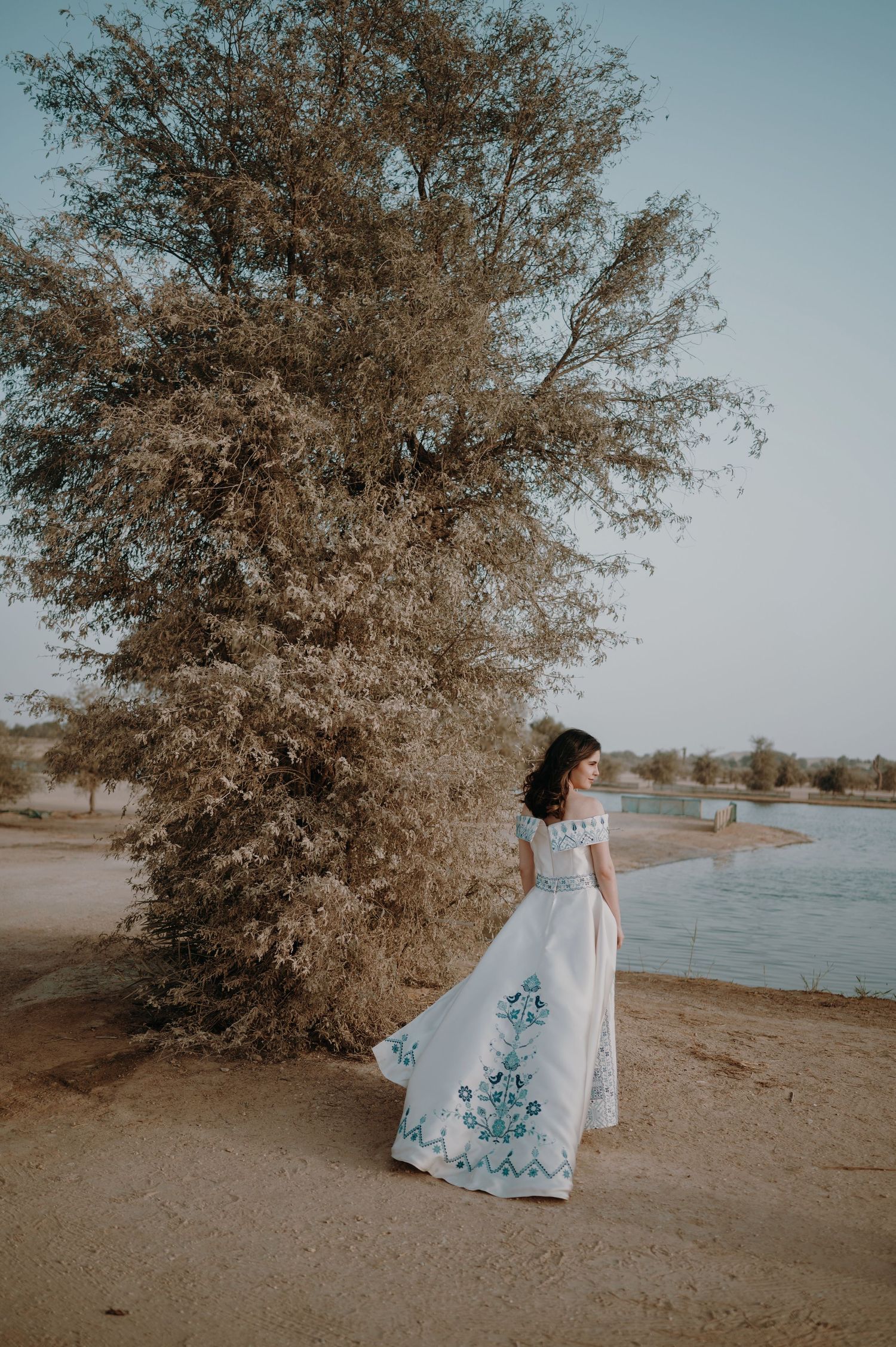 Wedding dress with blue details photographed against lakeside landscape and autumn trees.