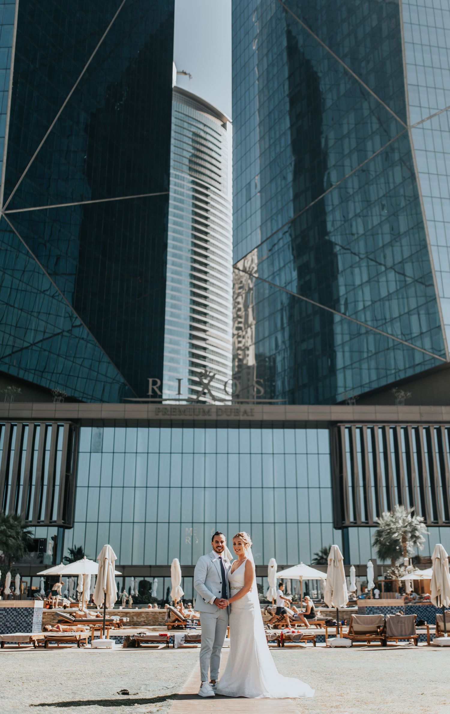 Wedding couple walking near modern glass buildings and outdoor lounge area.