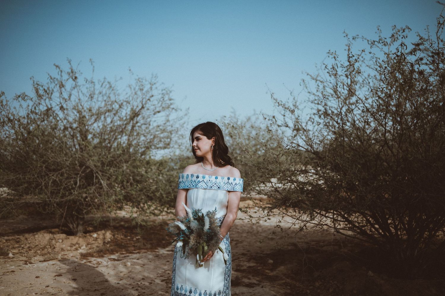 A romantic desert engagement photoshoot with a couple walking through brush.