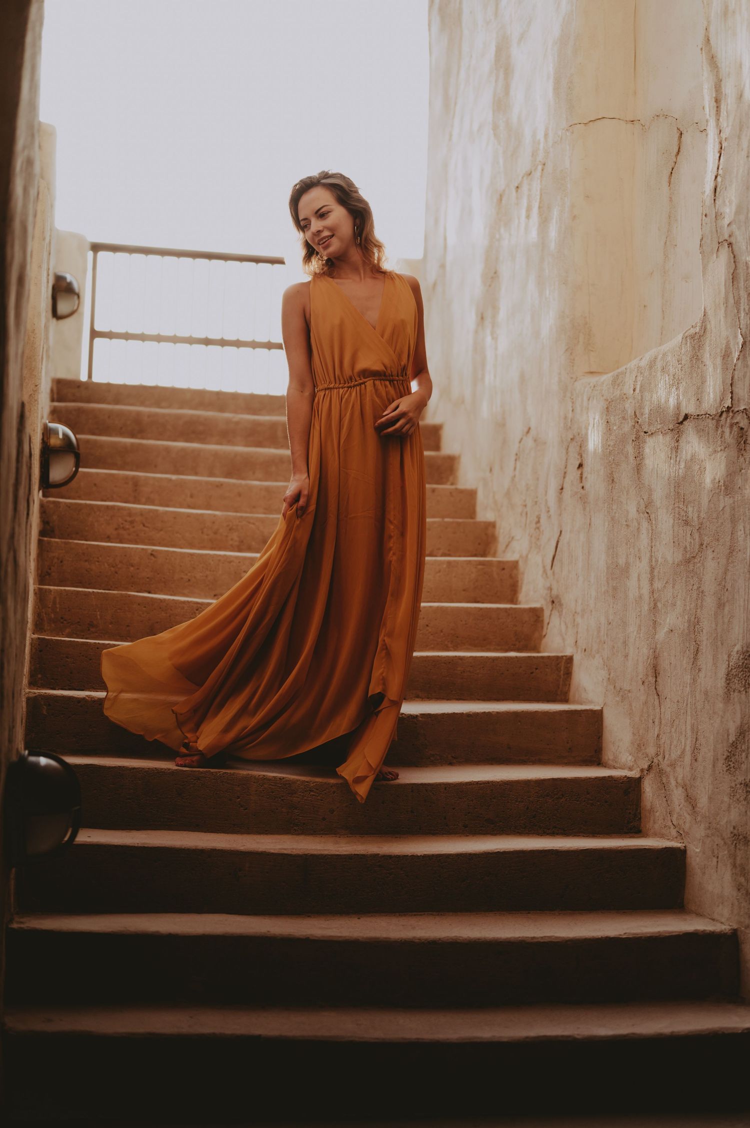 A flowing amber dress creates elegant movement along stone steps in dramatic lighting.