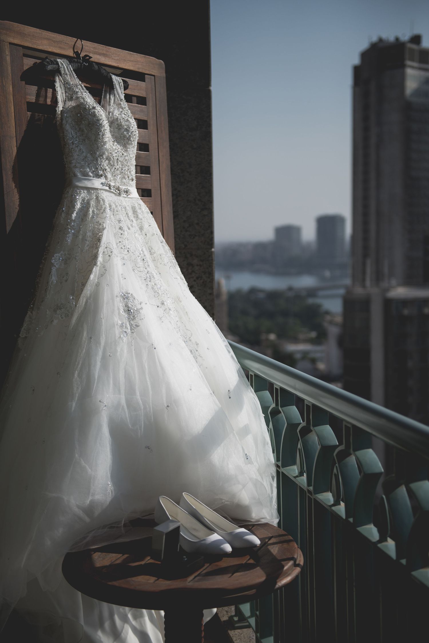 White wedding dress hangs on balcony with city skyline view in background.