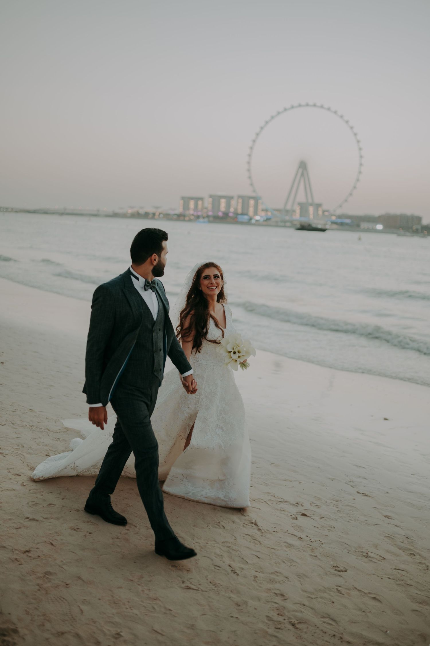 Couple walking along a misty beach with city skyline in the background.
