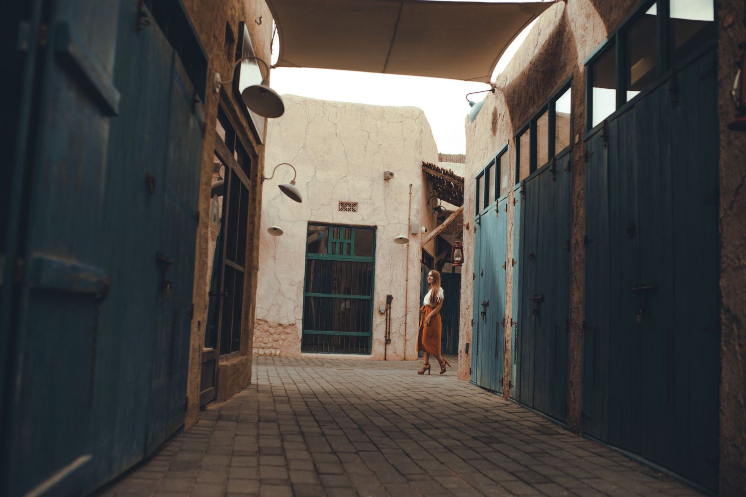 Long narrow alleyway with blue doors and white walls creates dramatic perspective.