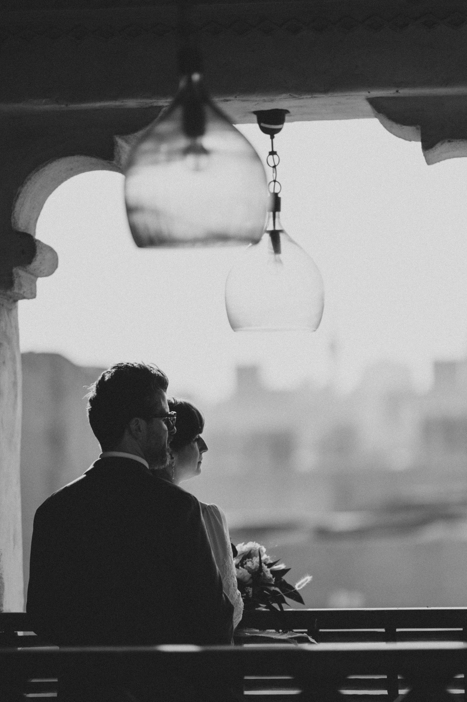 A silhouetted couple stands together against a bright window in an artistic black and white composition.