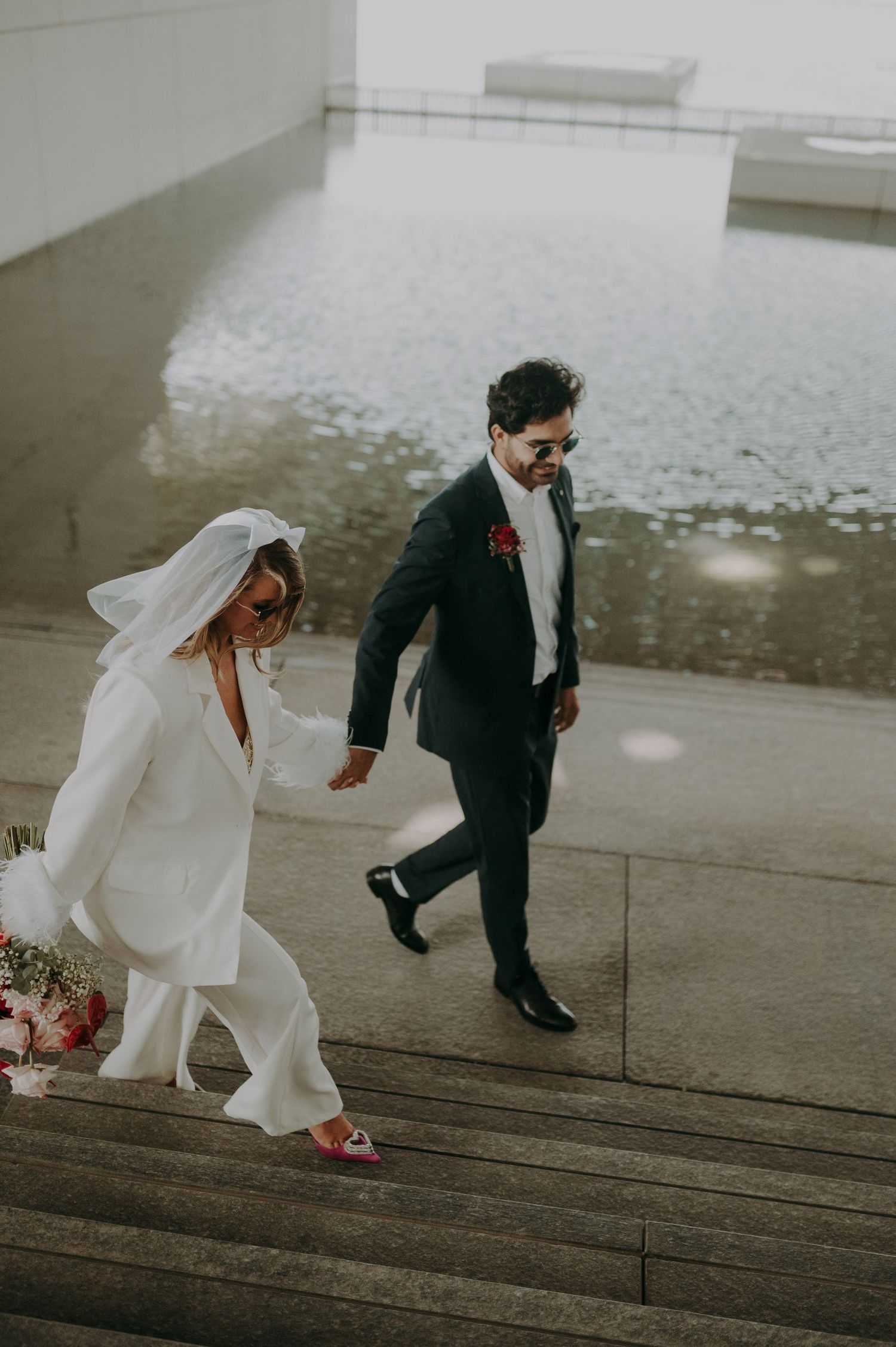 A couple descending concrete steps, with the bride in white and groom in black suit.