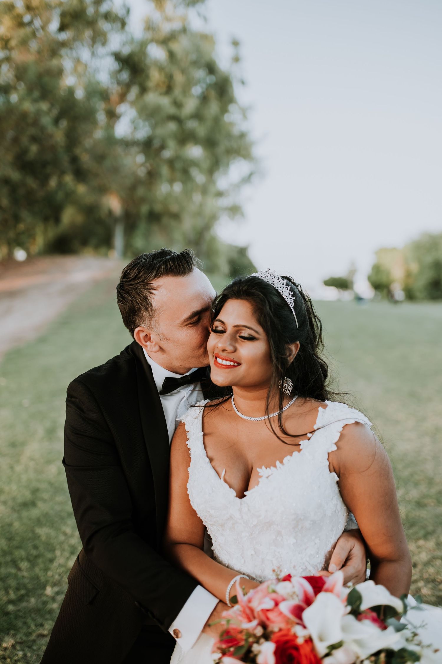 A romantic moment captured on a grassy hillside with a bouquet of red flowers.